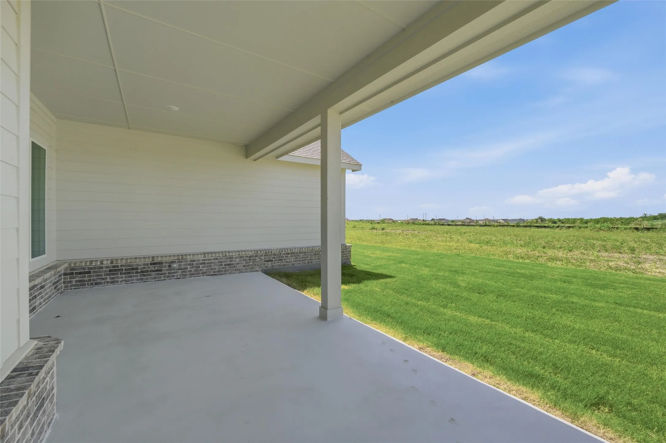 Covered patio with a concrete surface, white siding, and a brick veneer accent wall