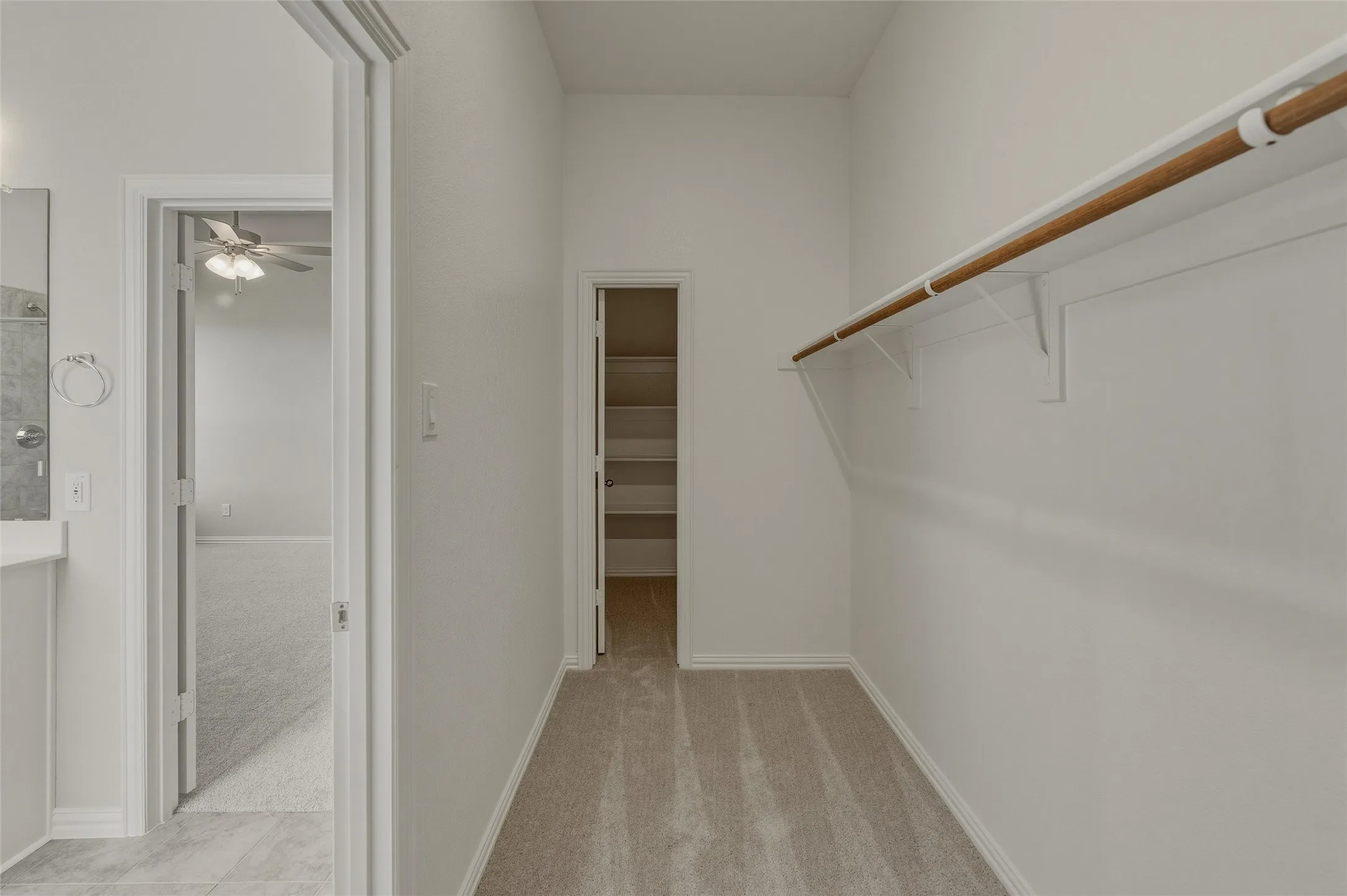 Neutral-toned carpeted closet featuring a built-in hanging rod and shelving system