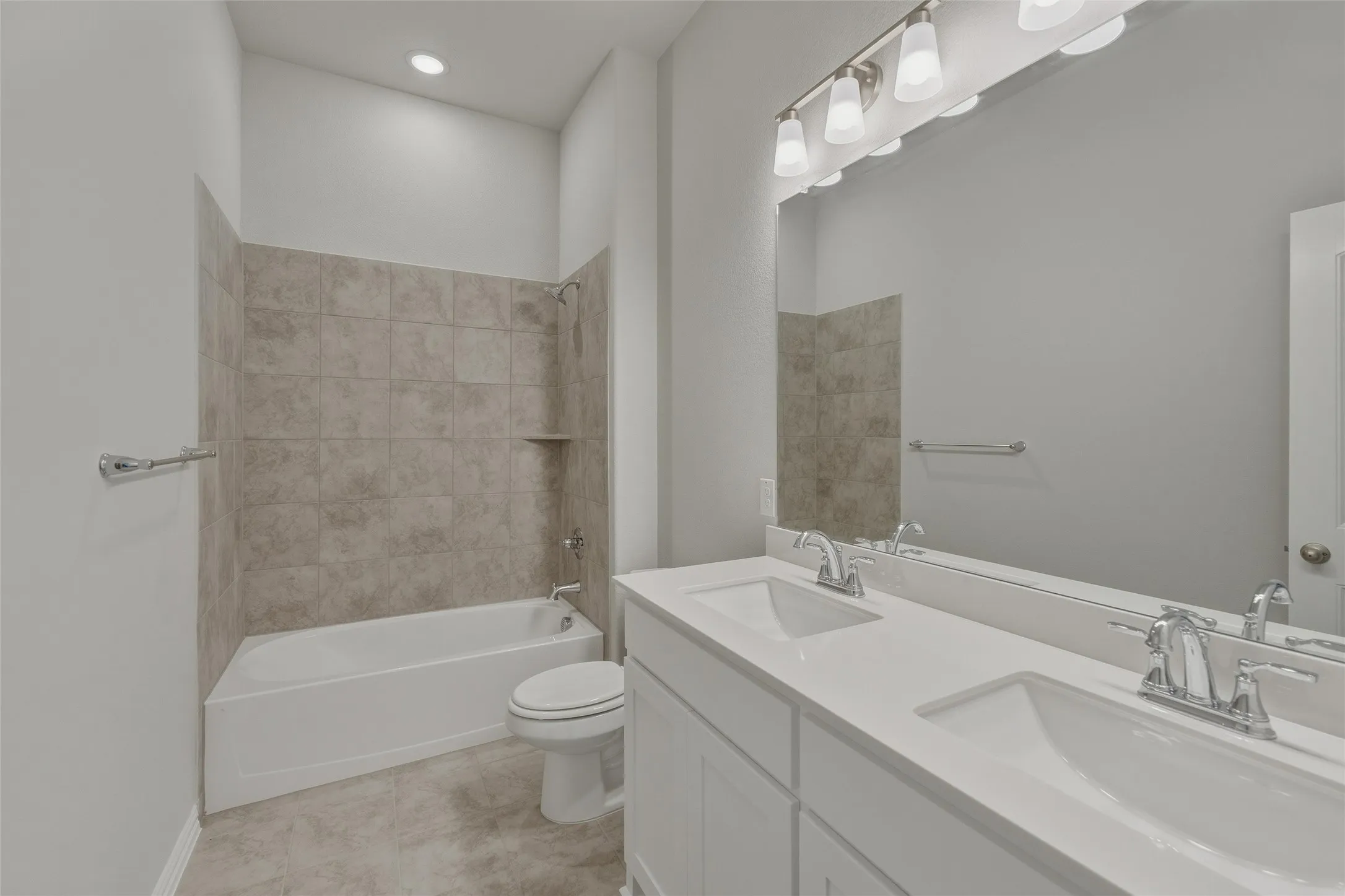 Bathroom featuring a dual-sink vanity with white countertops, a large vanity mirror, and a combination tub/shower with tiled surround and built-in shelving