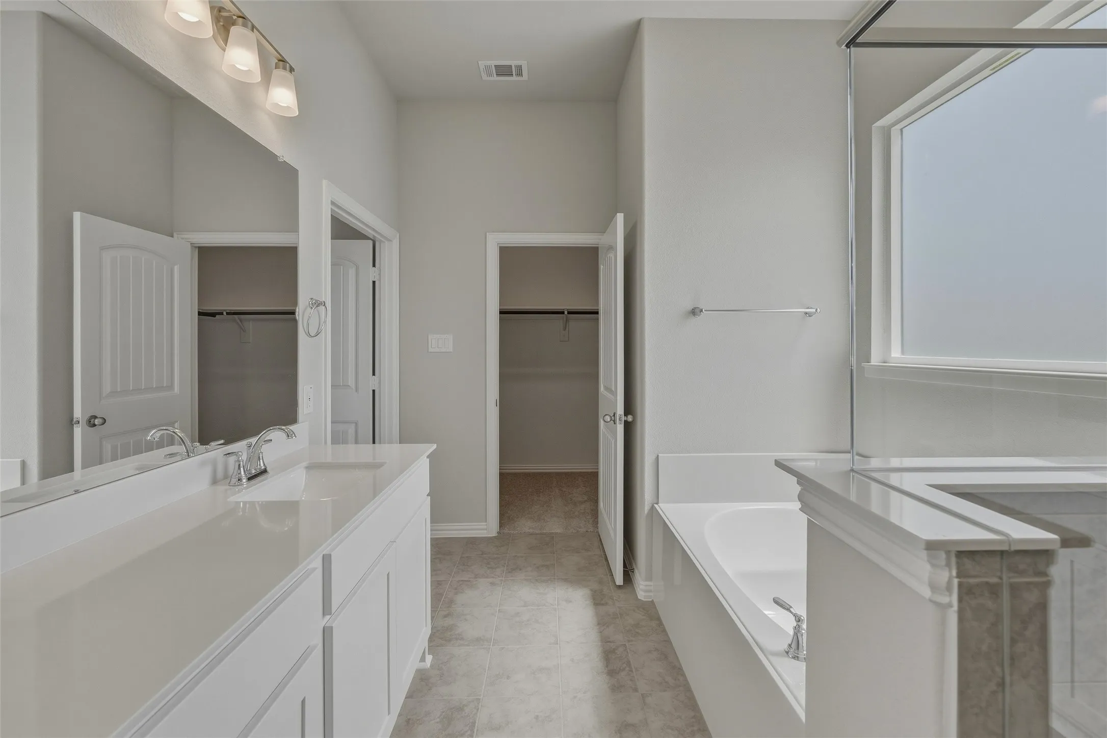 Bathroom featuring a double vanity with integrated sinks, a built-in soaking tub, a separate shower enclosure with a window, and a tile-finish floor