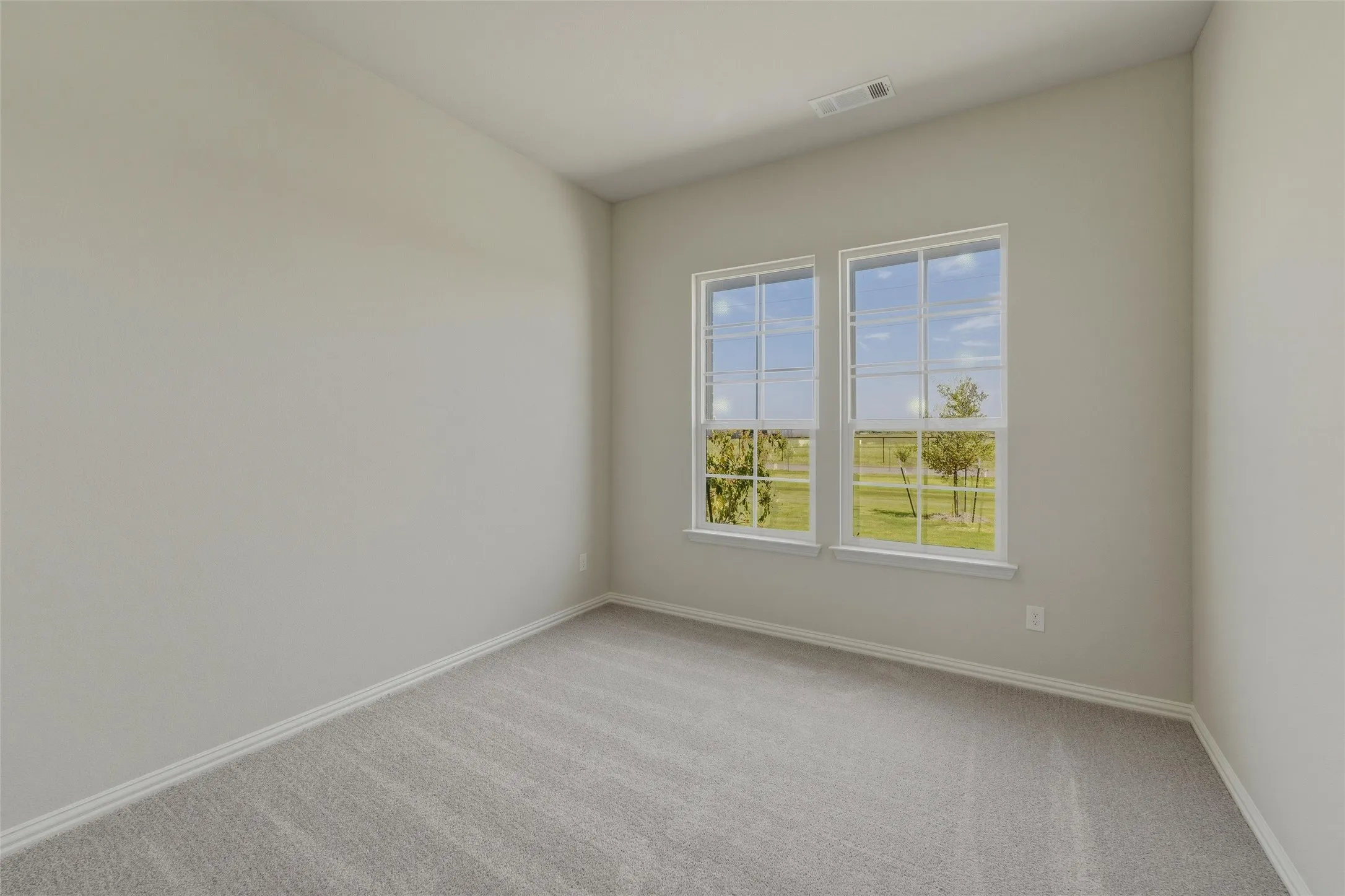 Bright interior space featuring two large windows with white trim, light gray carpeting, and neutral-toned walls
