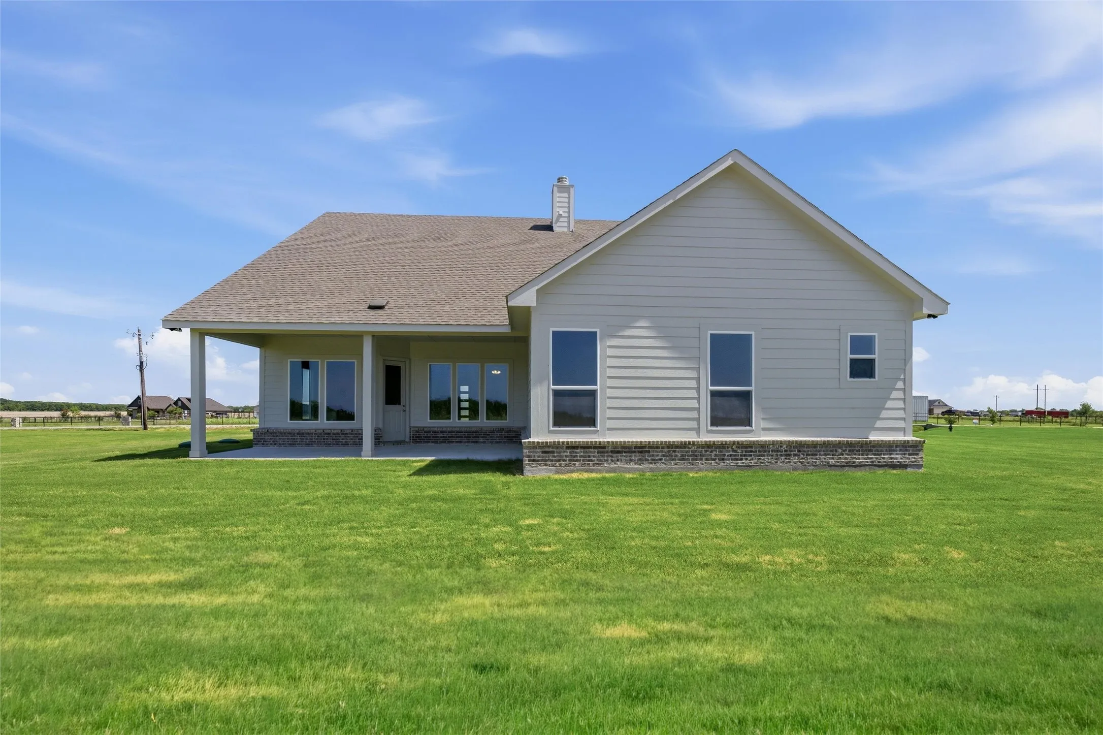 Rear exterior featuring a covered patio, multiple windows, light-colored siding, and a brick wainscoting foundation