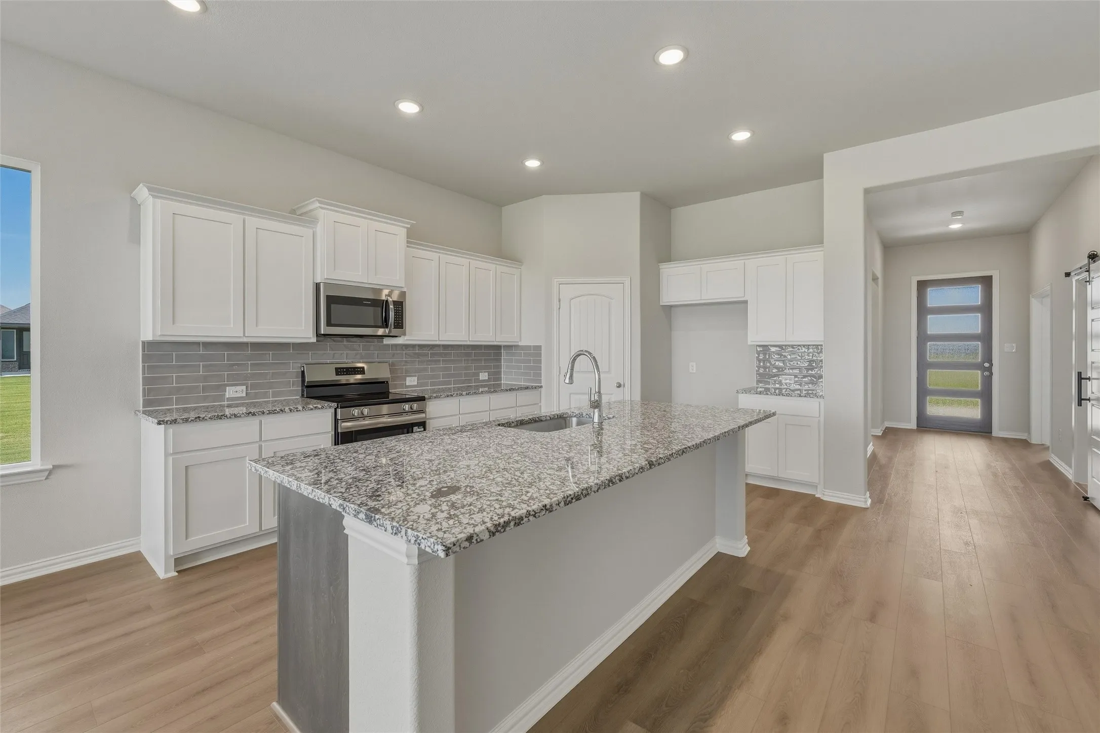Kitchen featuring a large central island with granite countertop, white cabinetry, stainless steel appliances, and a gray subway tile backsplash