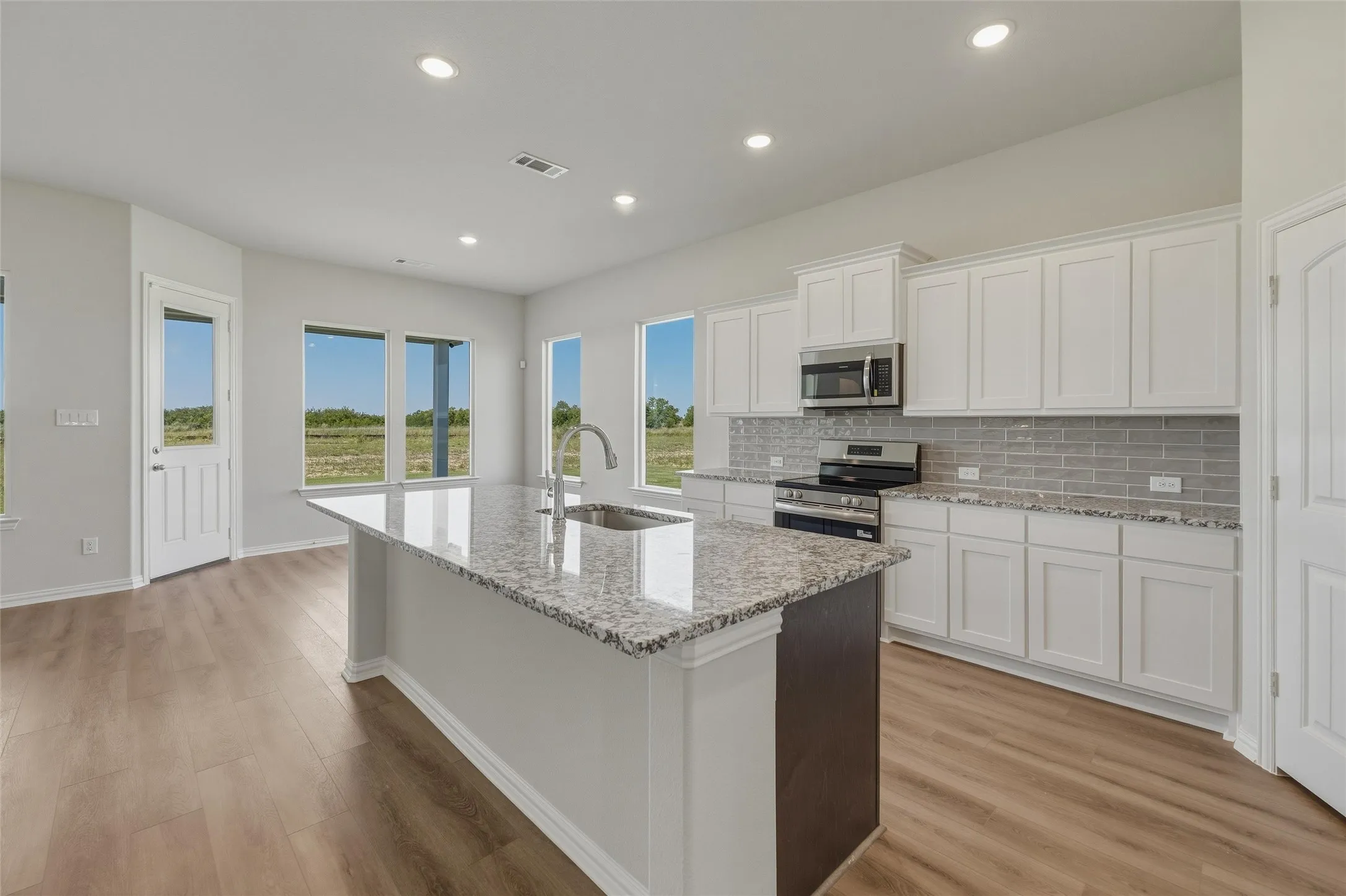 Kitchen featuring a large central island with a granite countertop and undermount sink, stainless steel appliances, white cabinetry, and wood-finish flooring