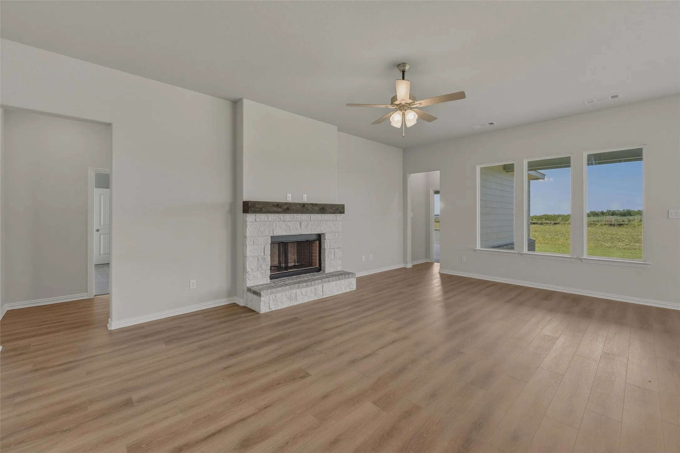 Spacious living area featuring wood-finish flooring, a white-painted brick fireplace with a wood mantle, and a ceiling fan