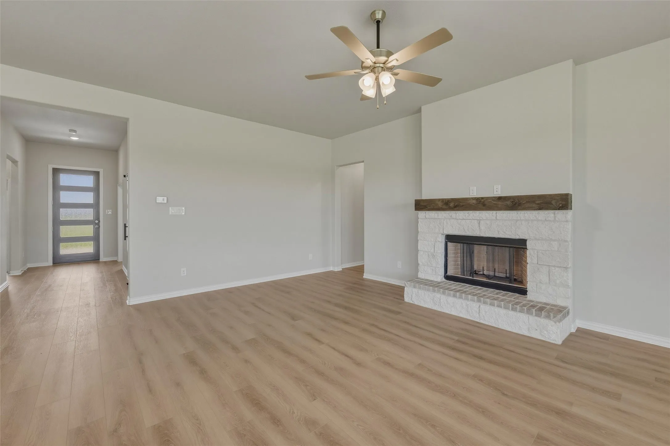 Spacious interior featuring wood-finish flooring, a contemporary ceiling fan, and a fireplace with a white stone surround and a wood mantel