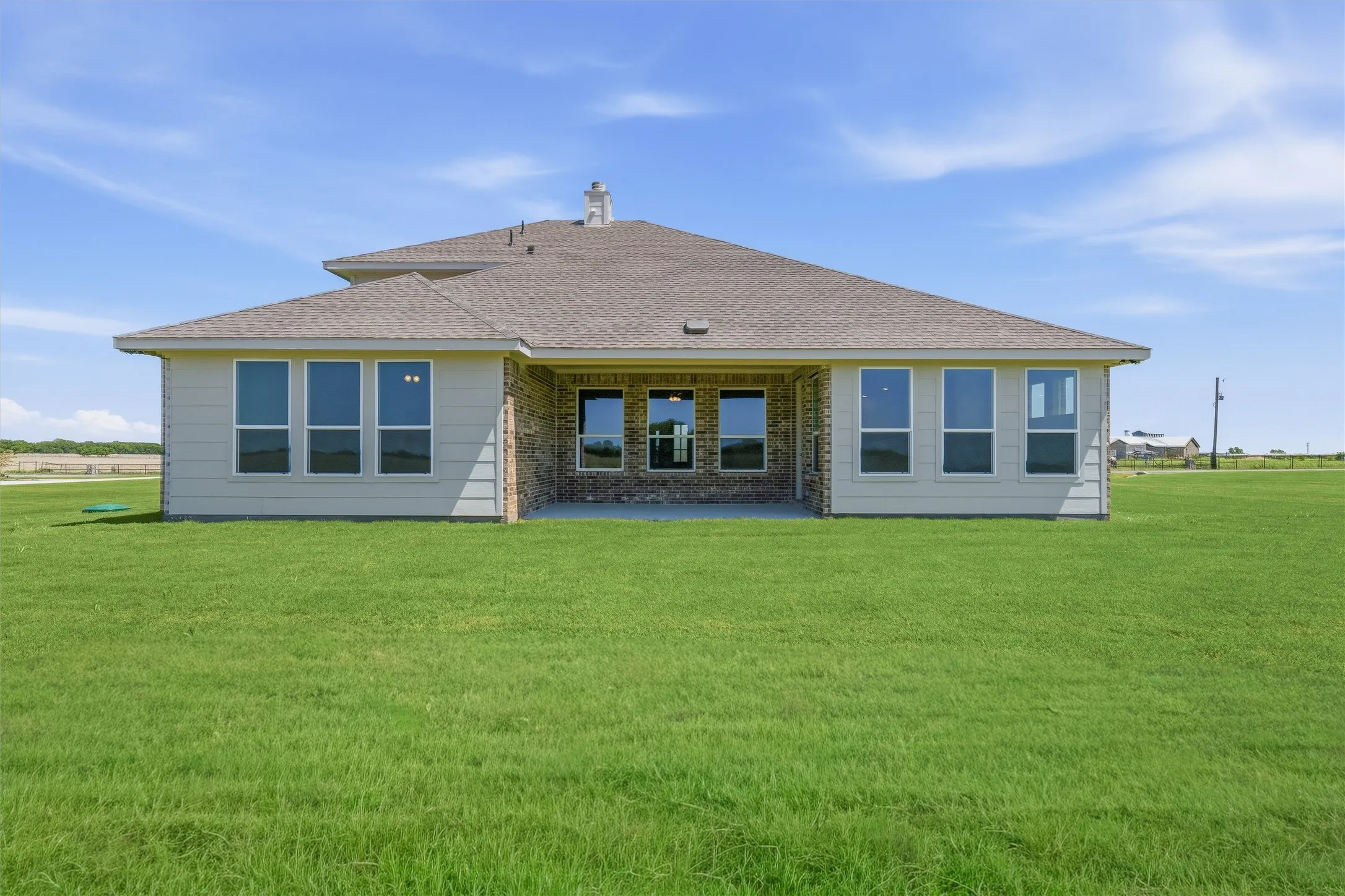 Rear exterior featuring a covered patio, extensive green lawn, light-colored siding, brick accent walls, and a shingle roof