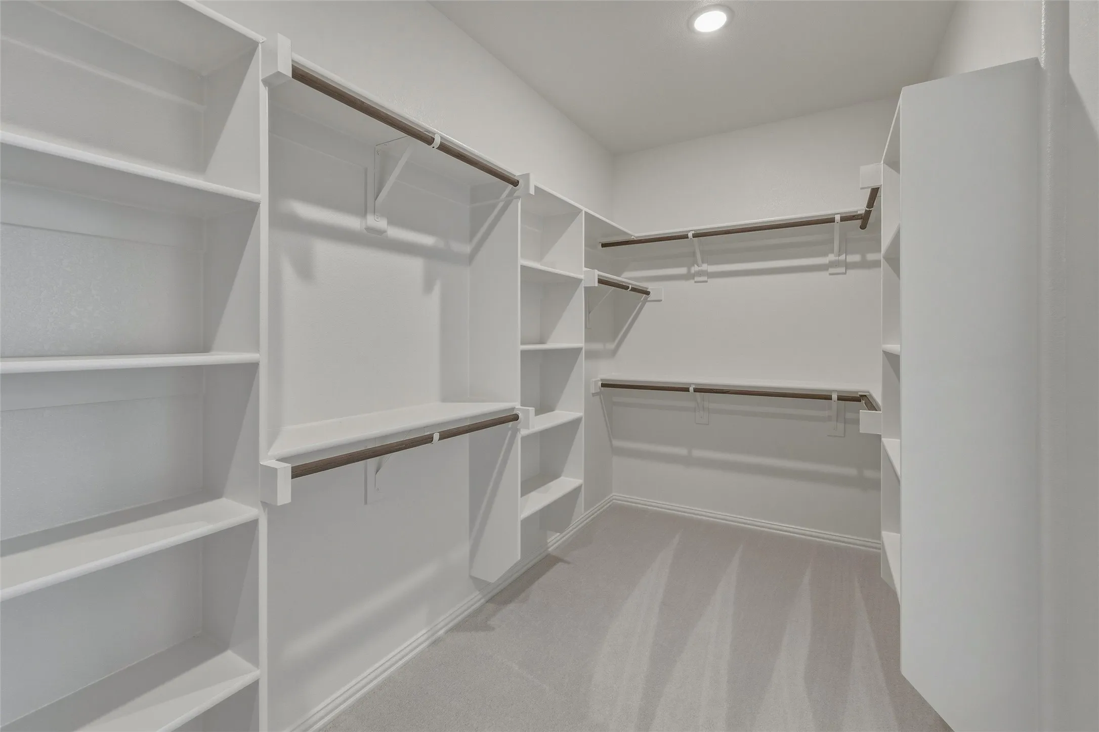 Spacious walk-in closet featuring extensive built-in shelving, multiple hanging rods, recessed lighting, and light-toned carpet flooring