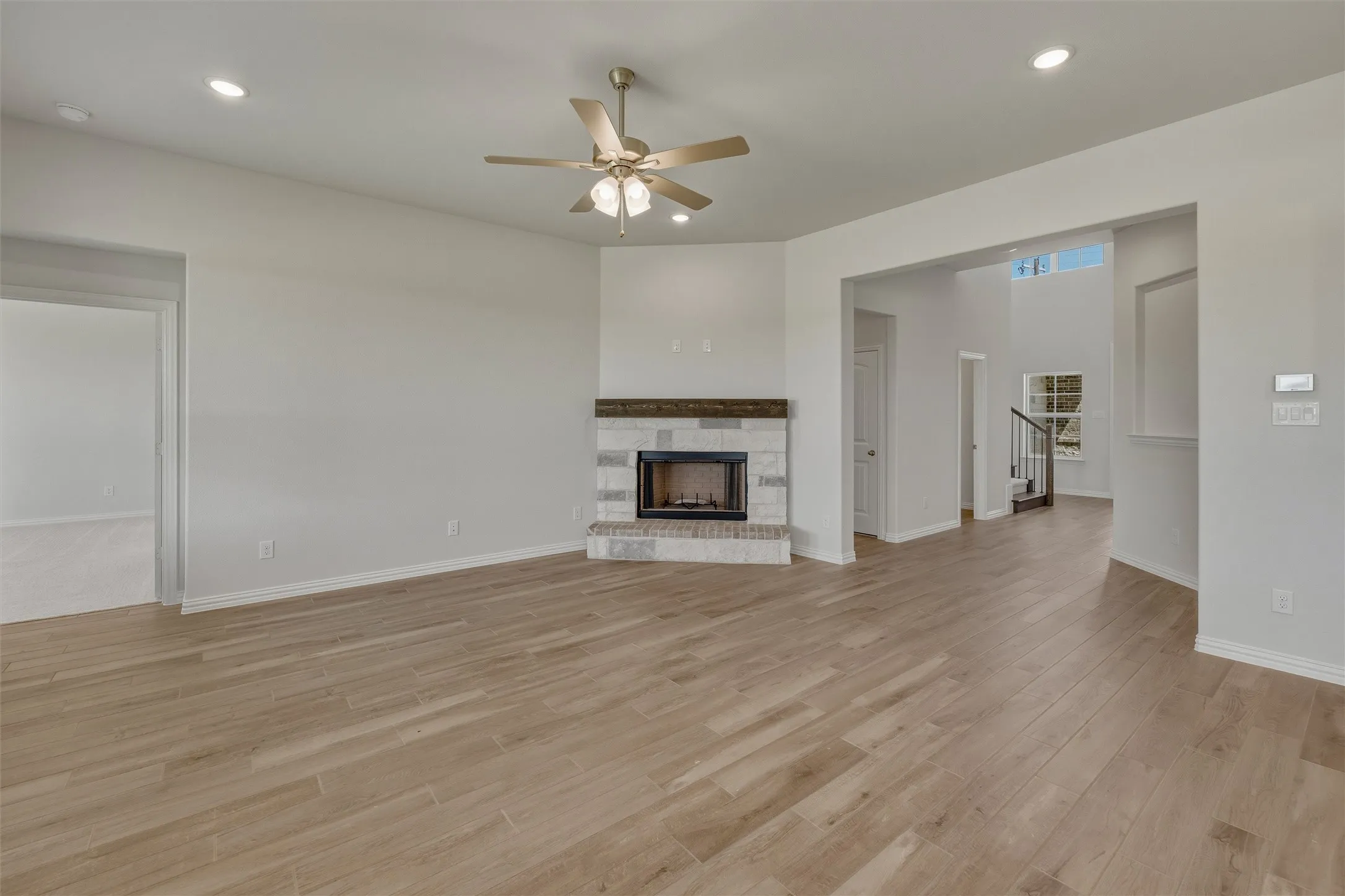 Spacious living area featuring wood-finish flooring, a corner fireplace with stone surround and wood mantel, recessed lighting, and a ceiling fan