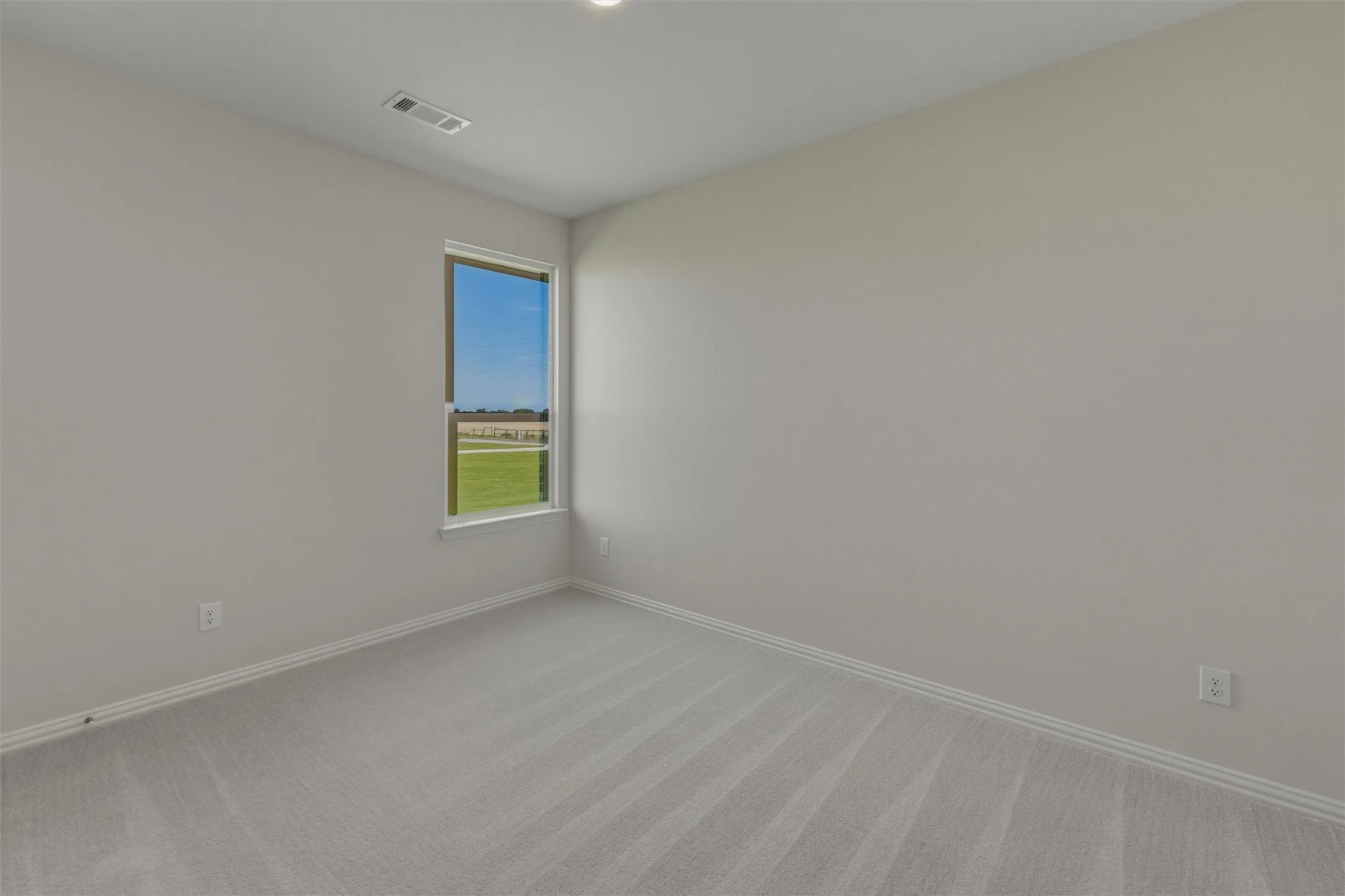 Spacious room featuring light gray wall paint, patterned gray carpeting, and white baseboards