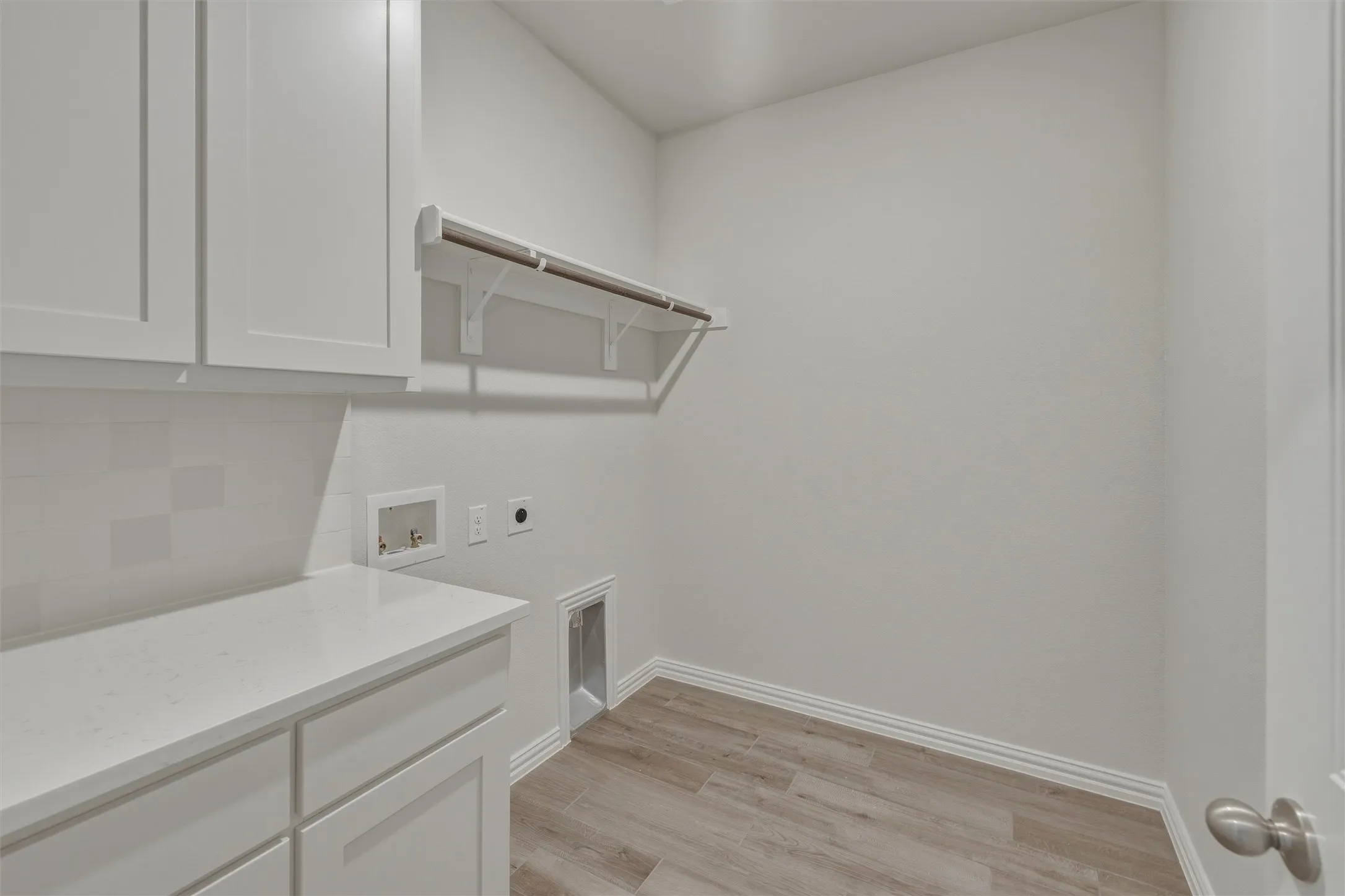 Utility room featuring wood-finish flooring, white cabinetry, a light-toned countertop, and a white subway tile backsplash