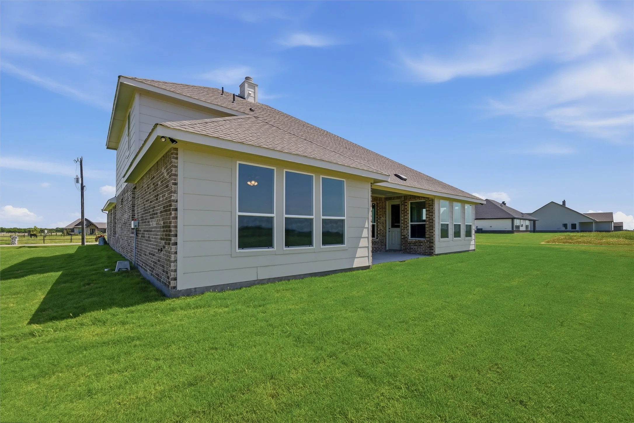 Expansive green lawn bordering the rear elevation, featuring a covered patio, multiple windows, and a brick and siding exterior