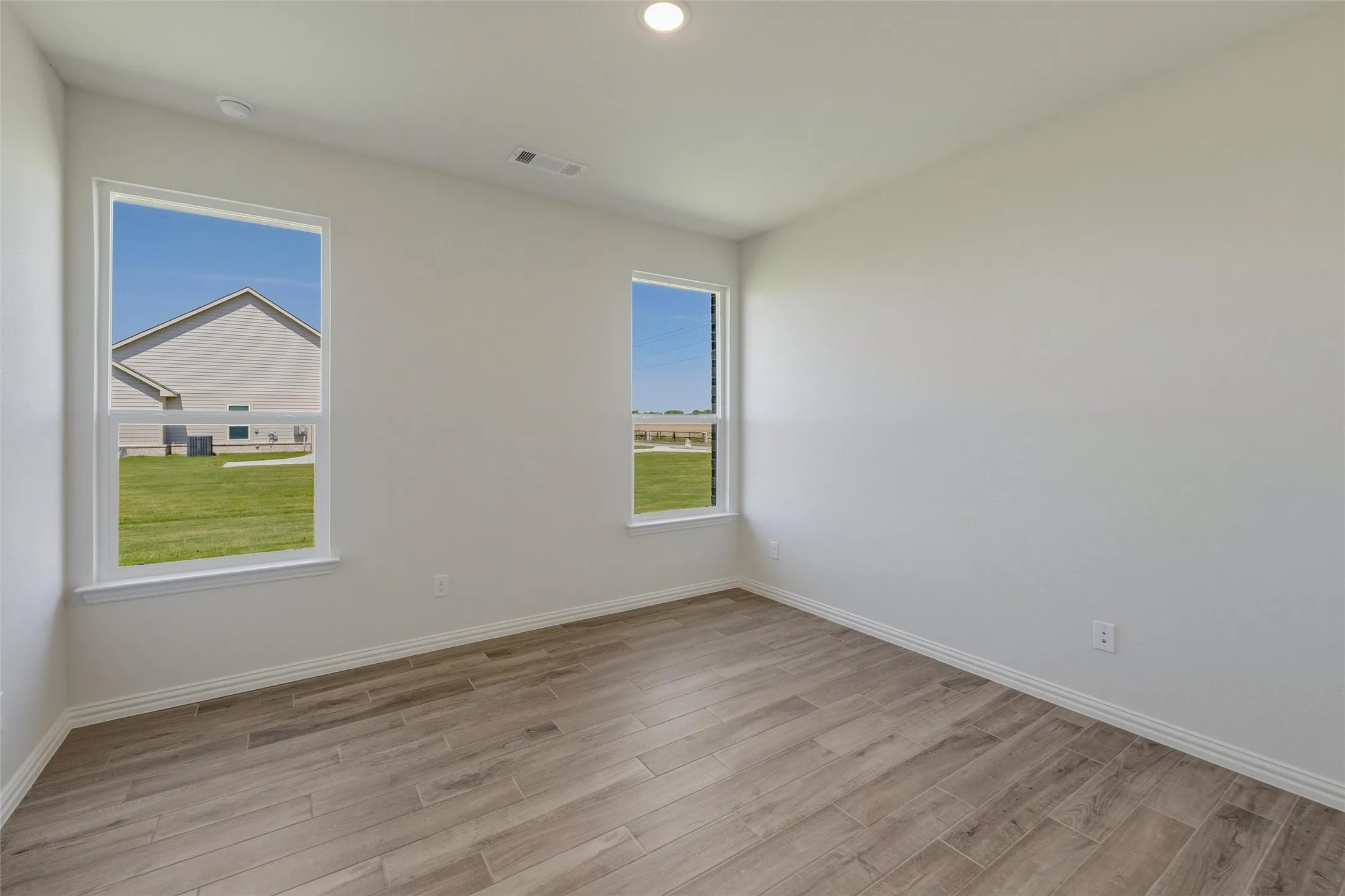 Spacious room featuring wood-finish flooring, two large windows, white baseboards, and neutral wall paint