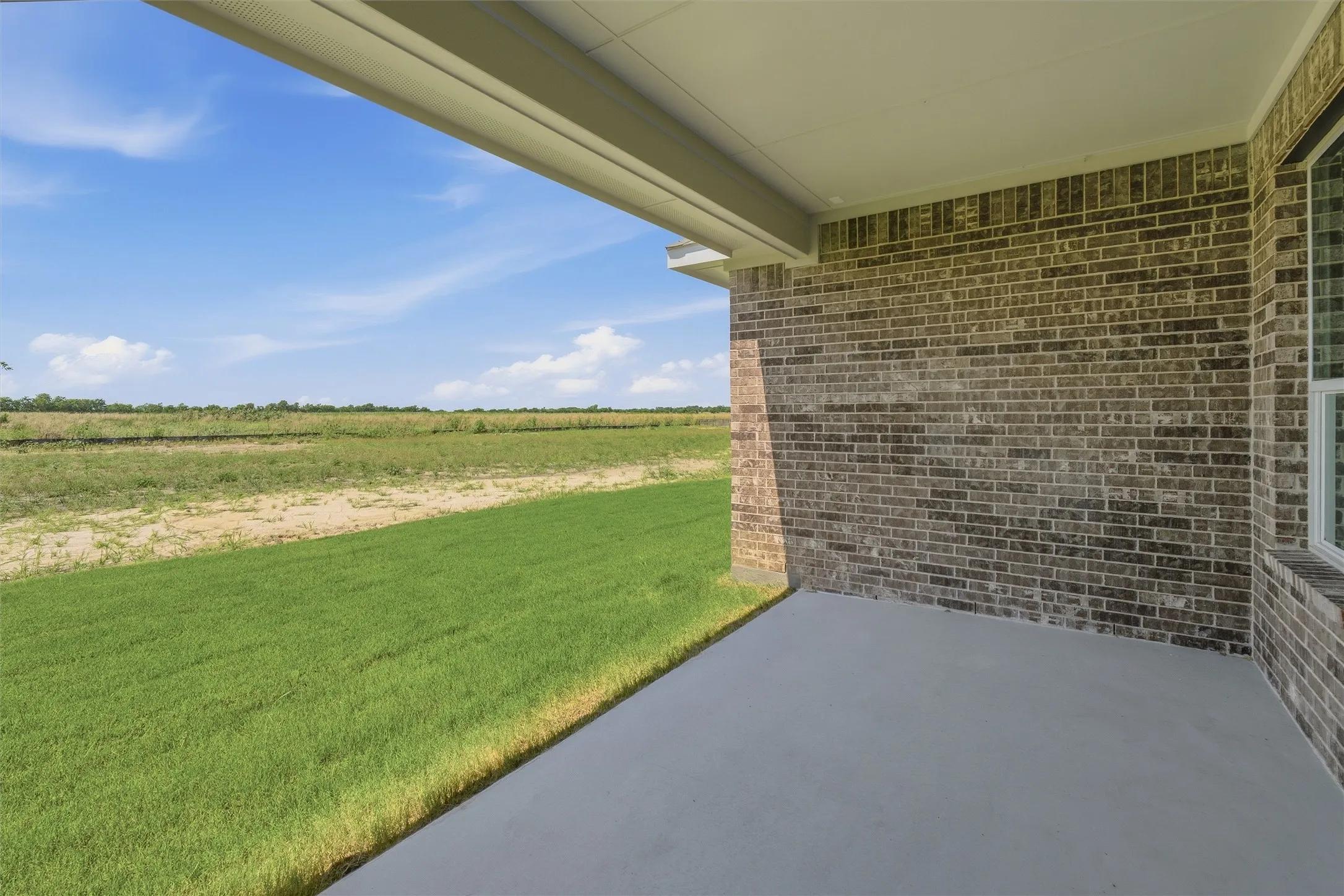 Covered concrete patio featuring a brick exterior wall and a window with white trim