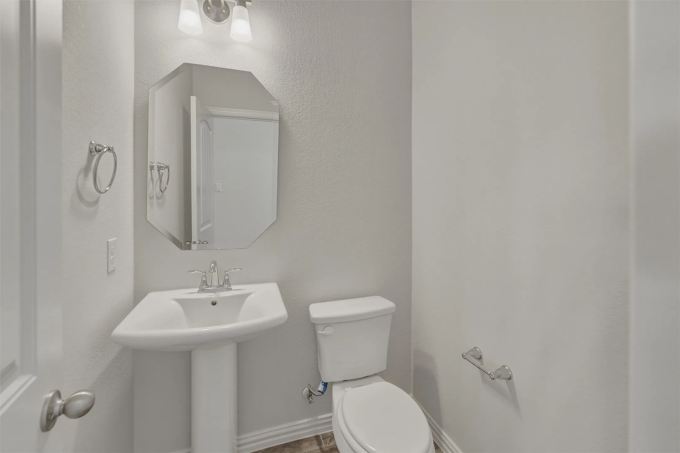Bright bathroom featuring a pedestal sink, brushed nickel fixtures, an octagonal mirror, and a two-piece toilet