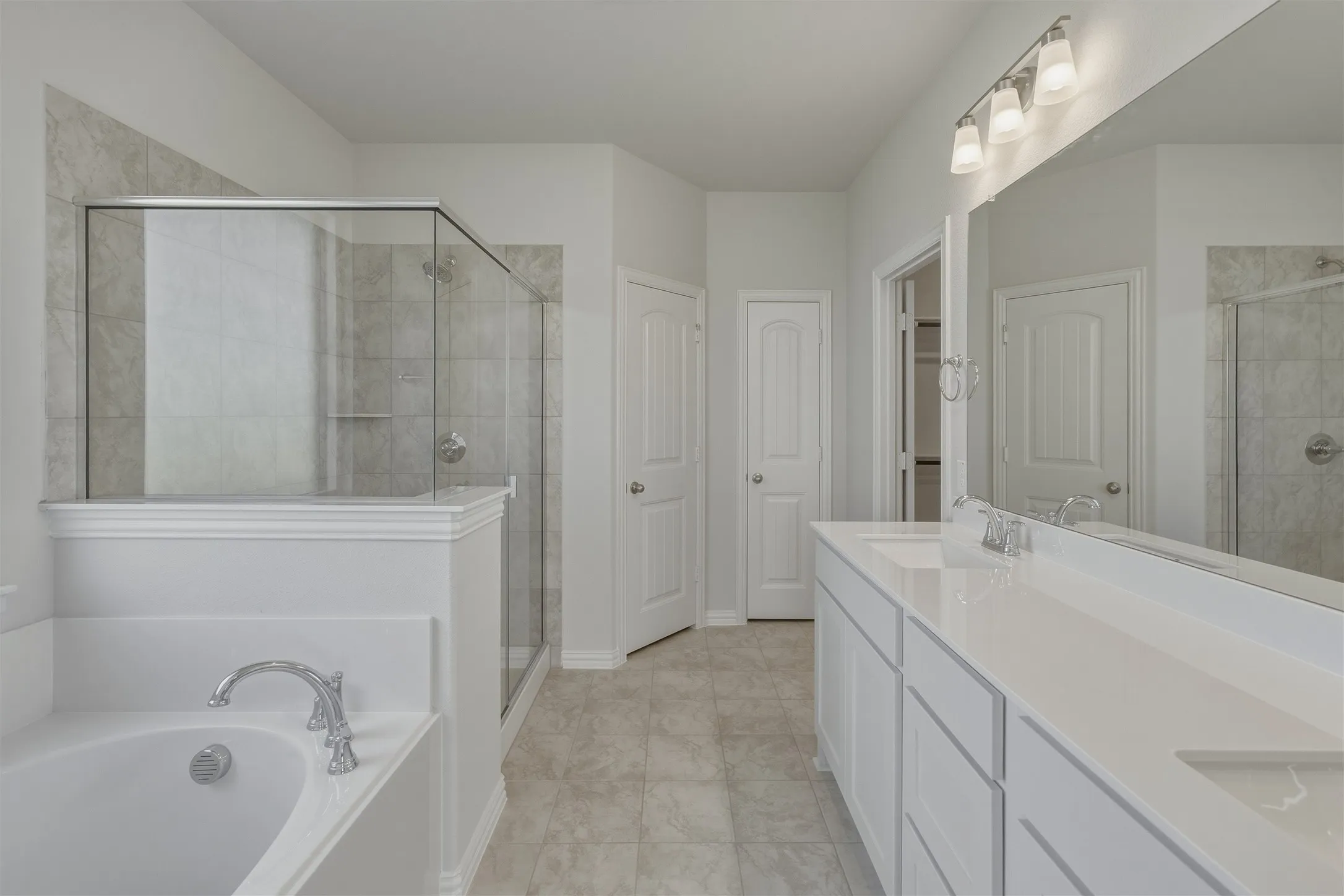 Bathroom with an oval soaking tub featuring chrome fixtures, a glass-enclosed shower with tiled walls, and a dual vanity with white cabinetry and an integrated countertop