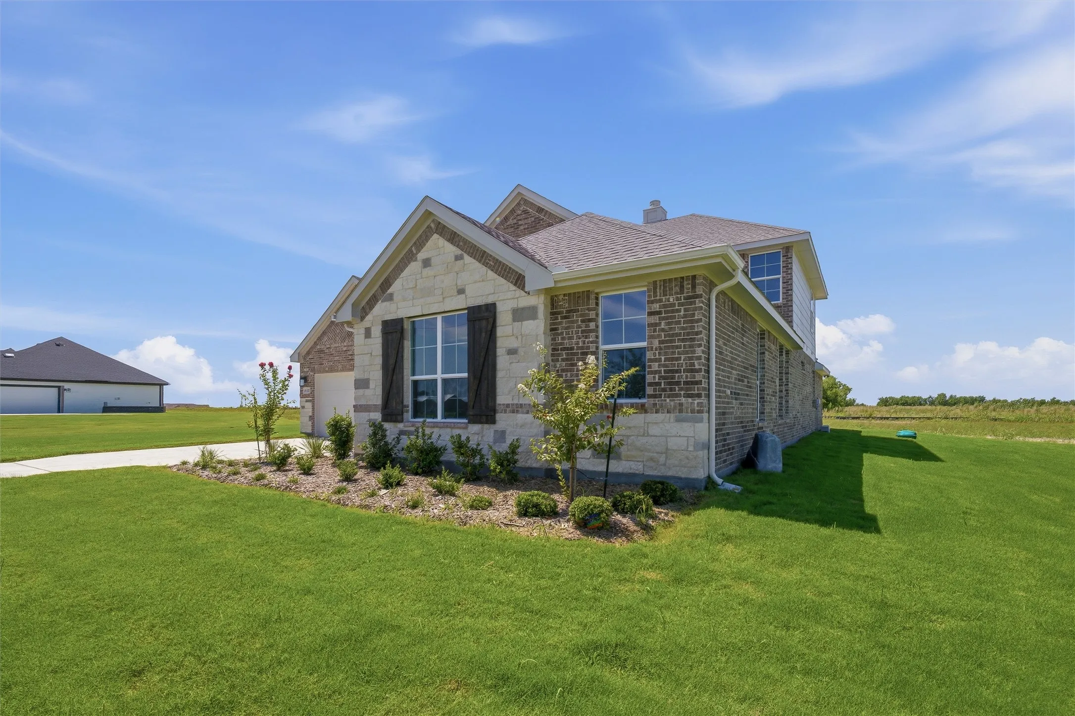 Brick and stone facade residence featuring a two-car garage, dark-stained shutters, and a well-maintained front lawn