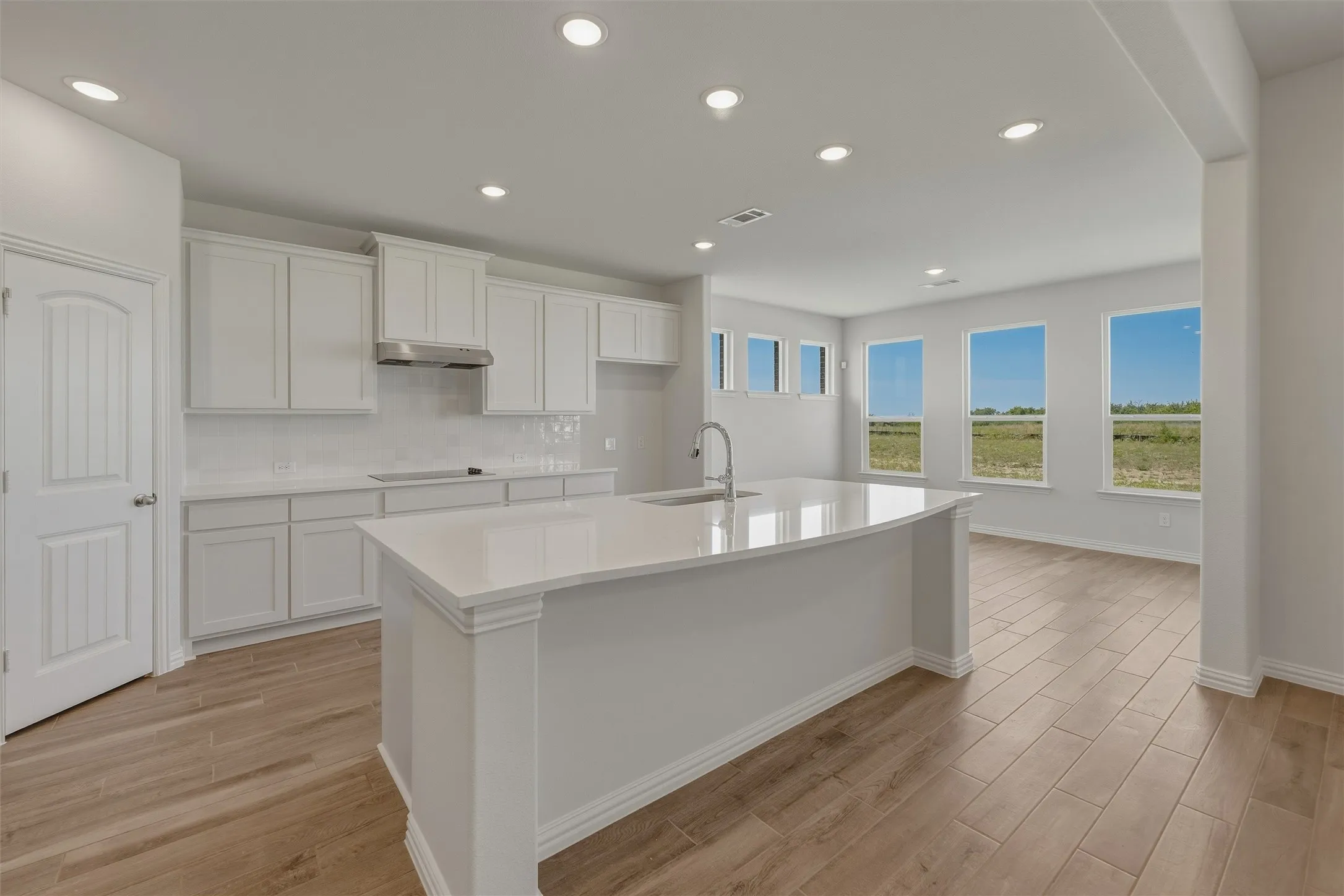Open-concept kitchen featuring an oversized island with an integrated sink, white shaker cabinetry, white subway tile backsplash, and stainless steel appliances