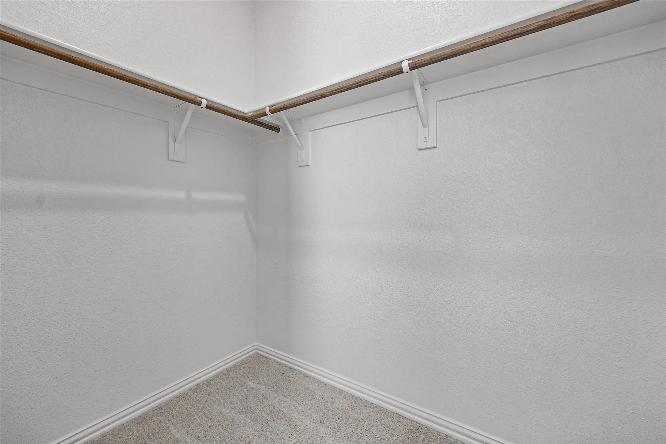 Corner closet with two wood-finish hanging rods, white wall brackets, and carpeting