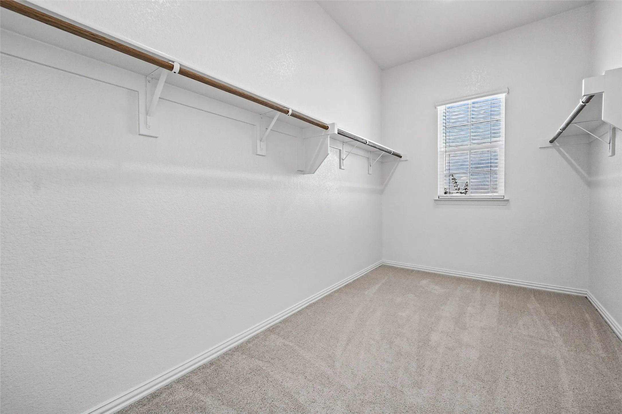 Built-in shelving and hanging rods, window with blinds, and light-toned carpet flooring