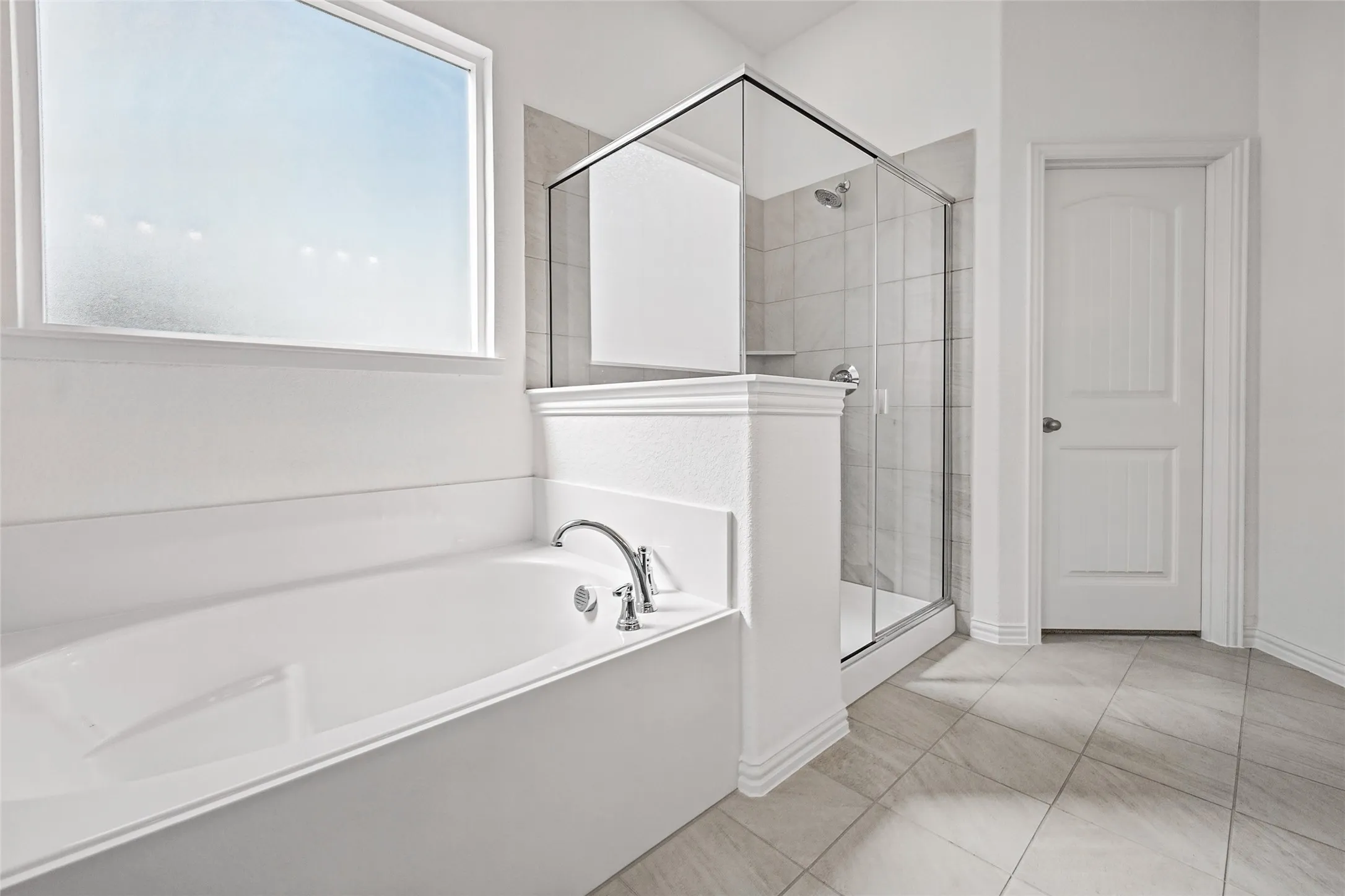 Soaking tub with polished chrome fixtures, separate glass-enclosed shower, tiled shower surround, and light-toned tile flooring
