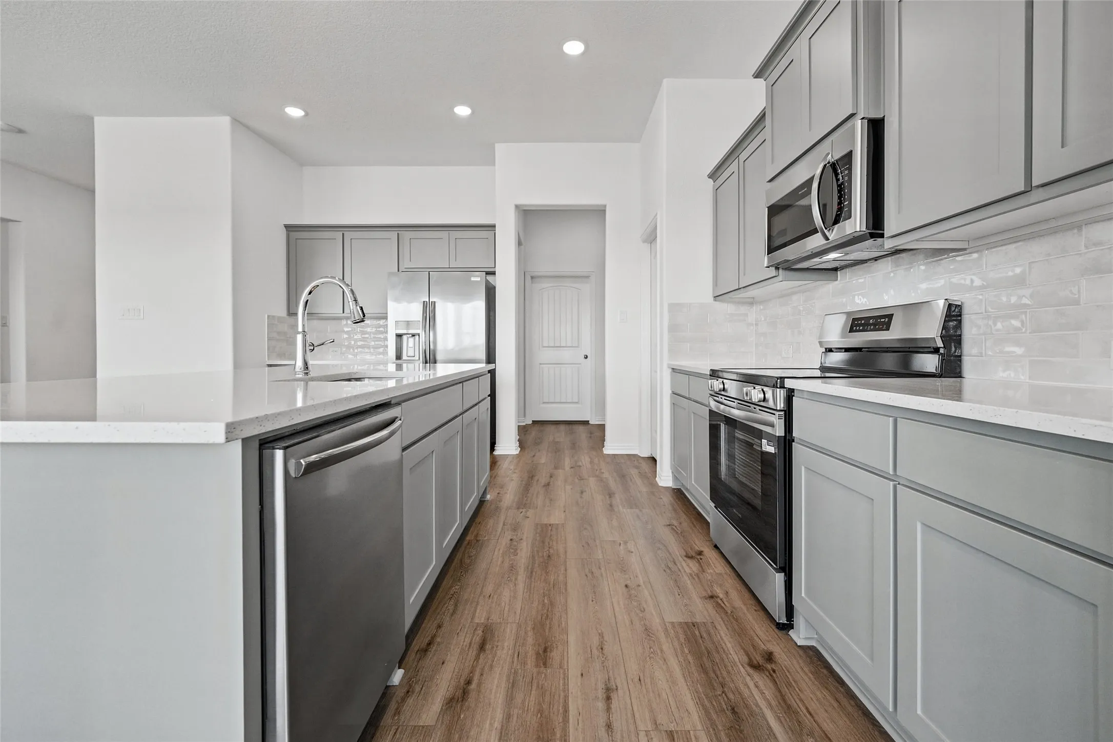 Kitchen featuring a stainless steel appliance package, light gray cabinetry, light-toned countertops, tile backsplash, and wood-finish flooring