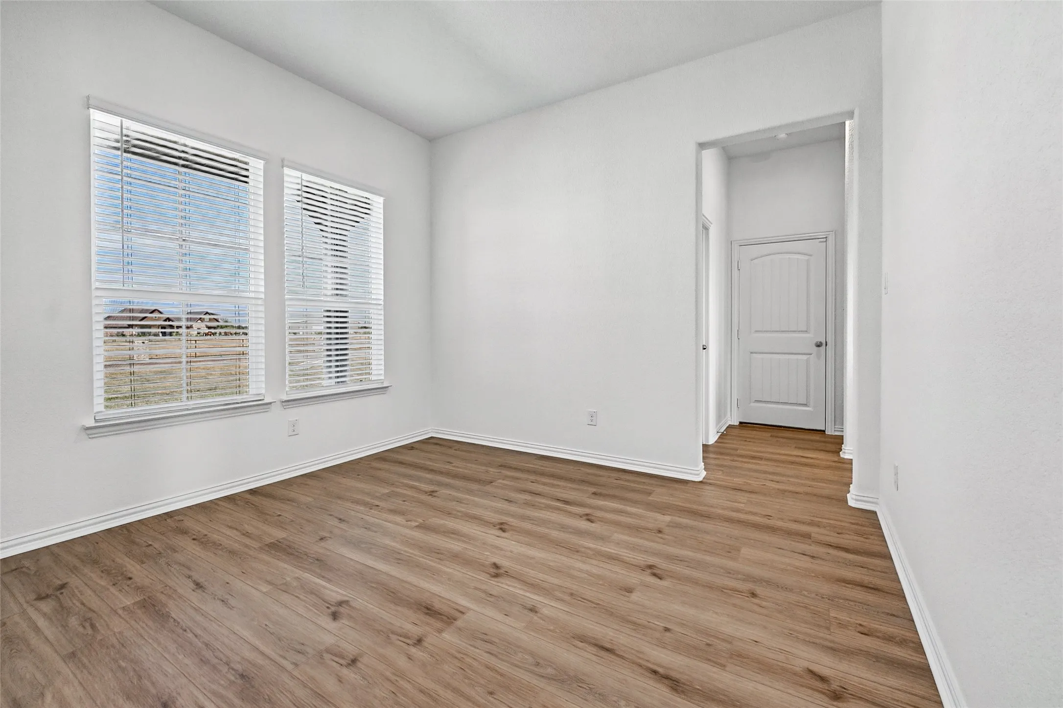 Room with wood-finish flooring, white walls, and two windows