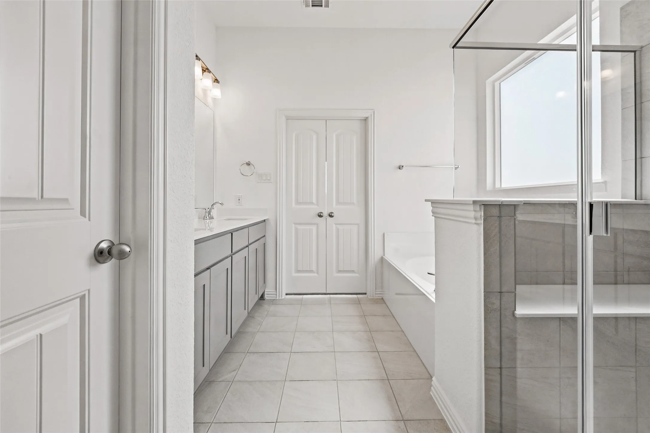 Dual vanity with undermount sinks, separate soaking tub, walk-in shower with glass enclosure, and tile flooring