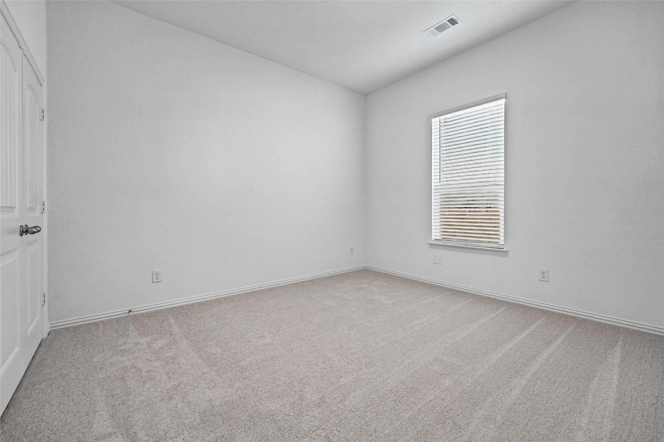 Carpeted room featuring a white paneled door, a single window with blinds, and white walls
