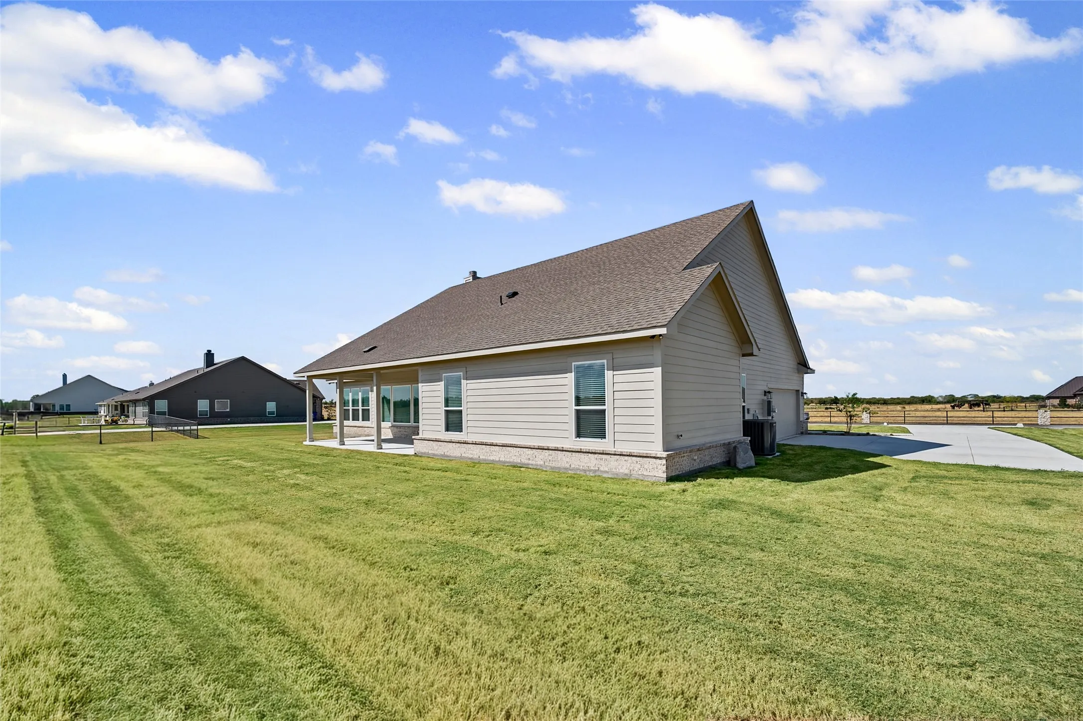 Spacious rear yard with a covered patio, multiple windows, and a concrete driveway