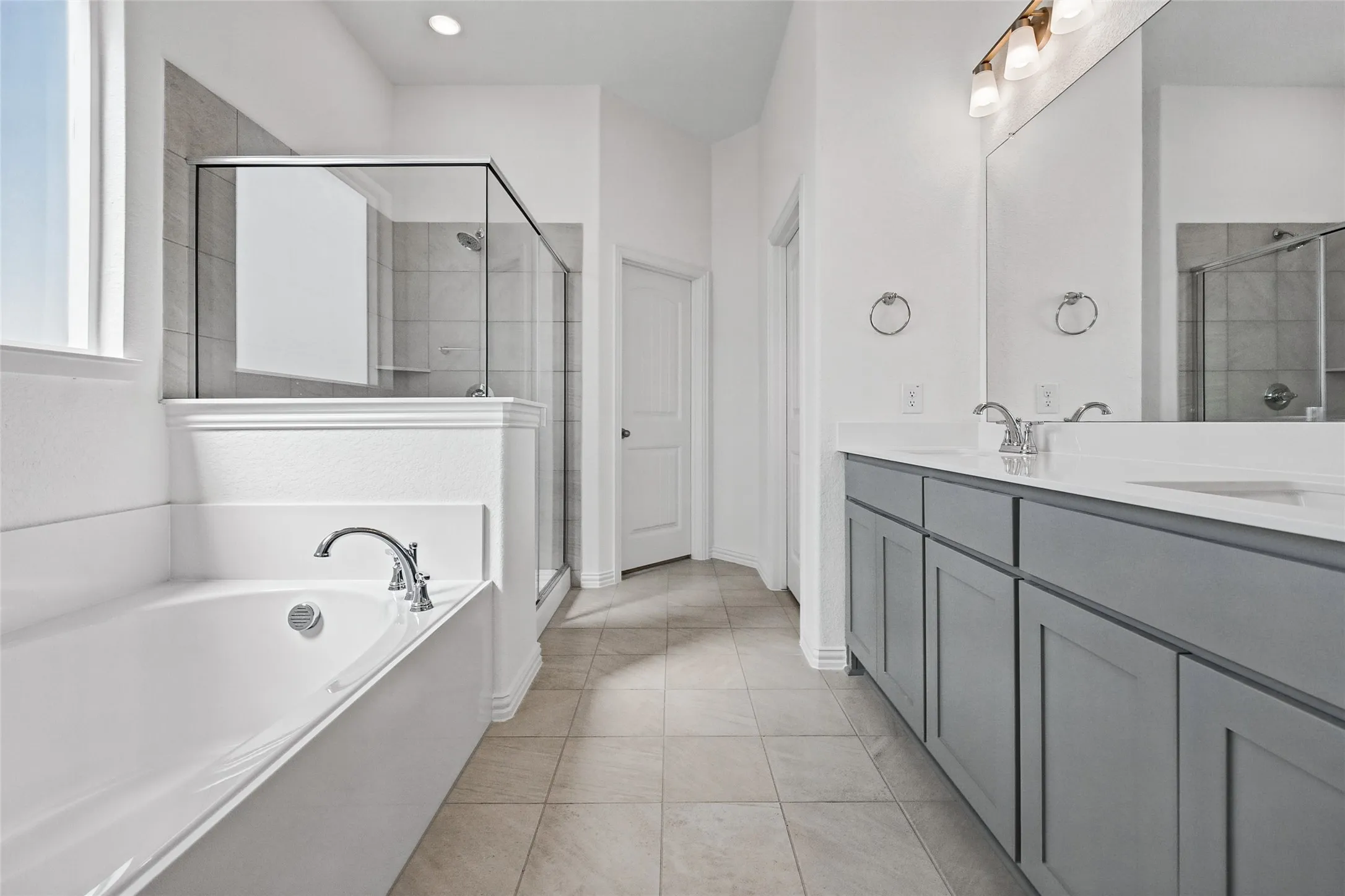 Bathroom featuring a built-in bathtub, glass-enclosed shower with tile surround, dual vanity with undermount sinks, and tile flooring