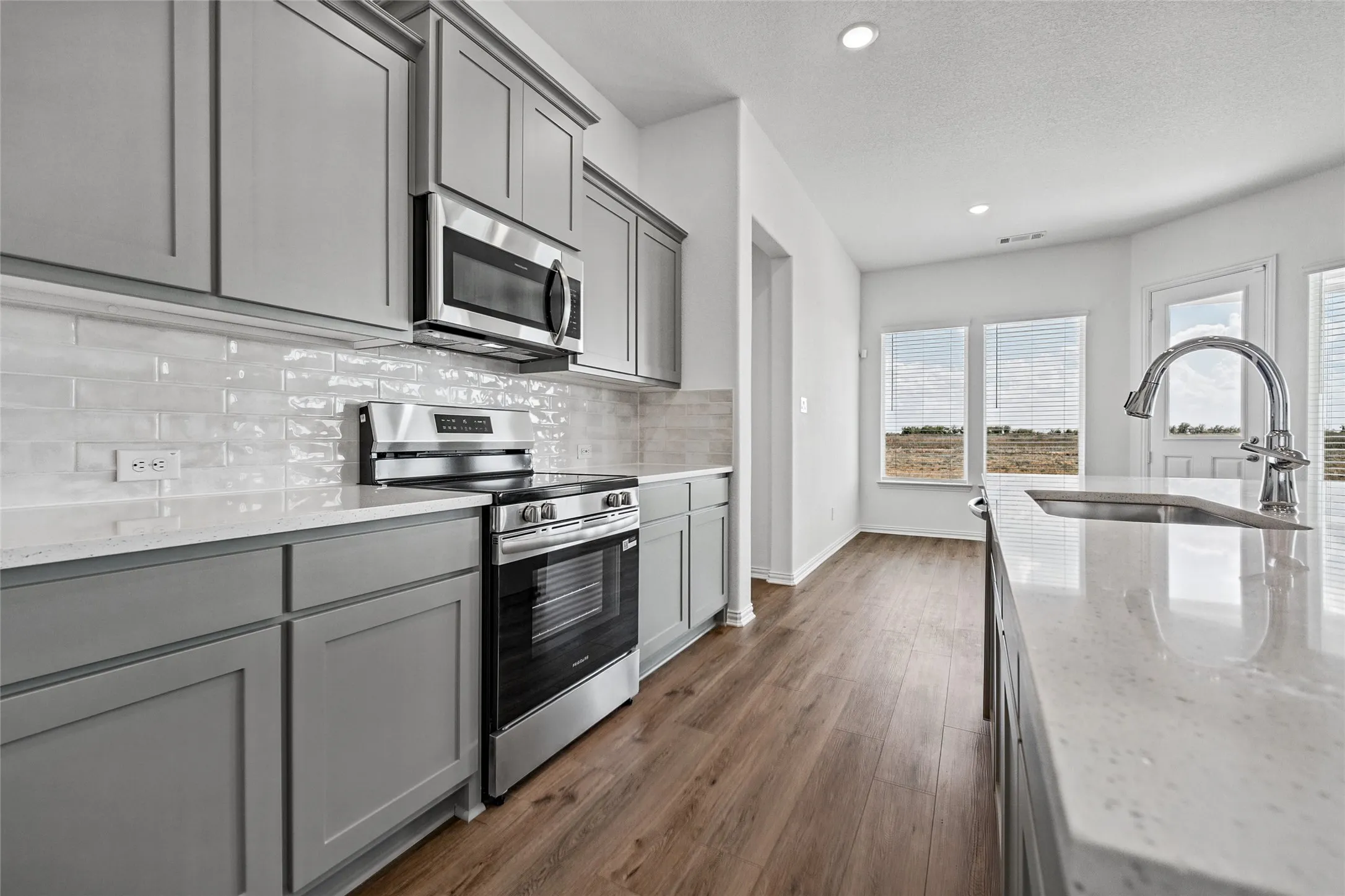 Kitchen featuring gray cabinetry, stainless steel appliances, a subway tile backsplash, light-toned countertops, and wood-finish flooring