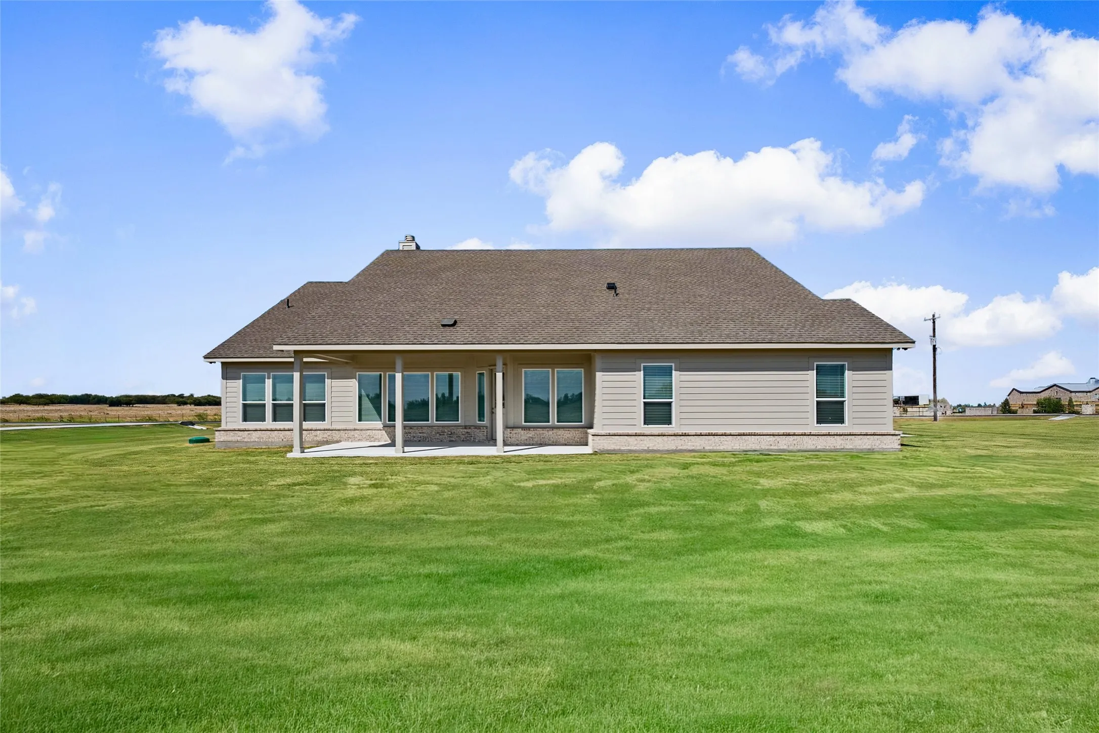 Expansive green lawn surrounds the residence, featuring a covered patio with columns and a shingle roof