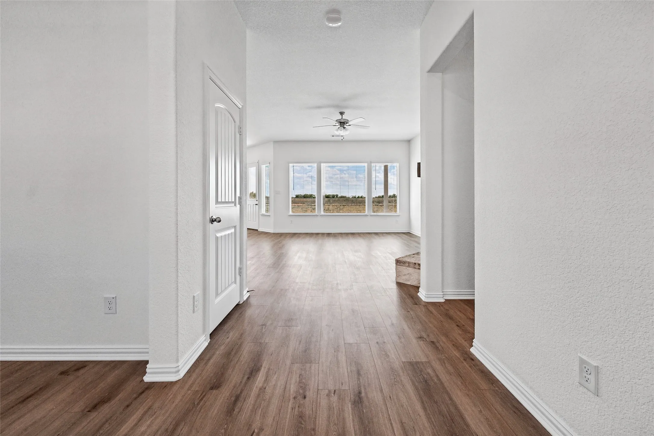 Wood-finish flooring throughout, white interior doors, multiple large windows, ceiling fan with light fixture, and white wall finishes