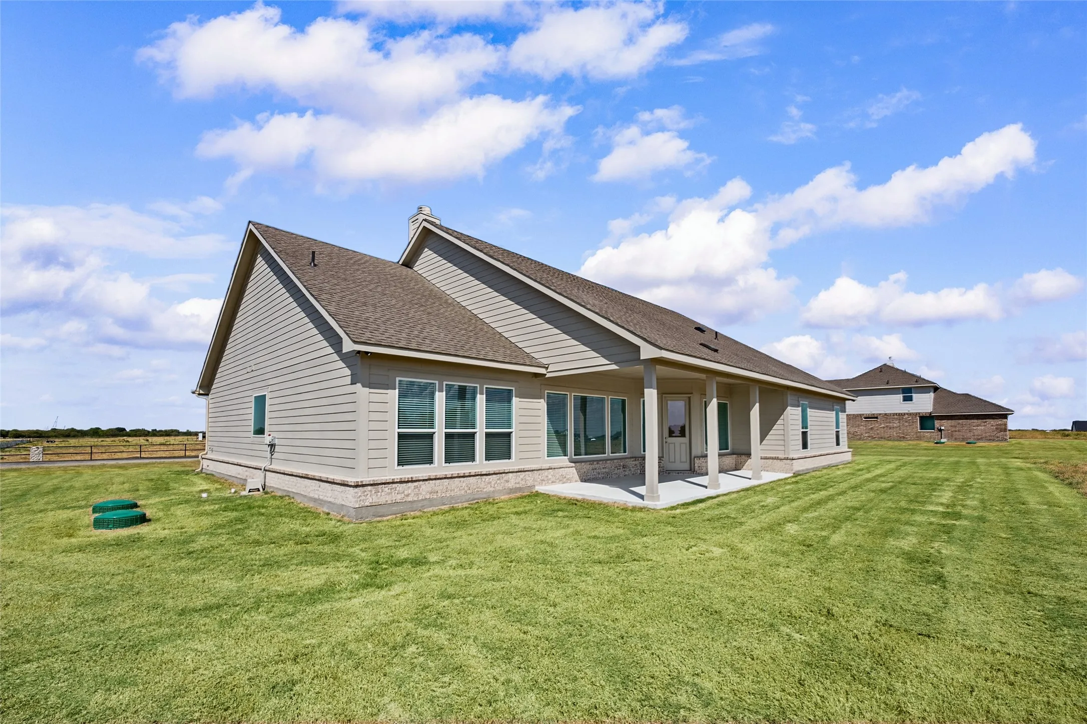 Expansive green space featuring a covered patio, multiple windows, and a brick skirt foundation