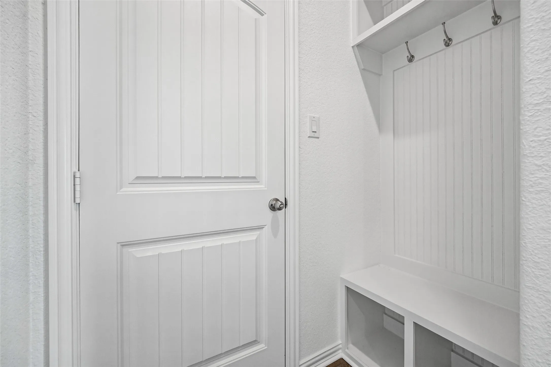 White paneled door, built-in storage bench with cubbies, beadboard wall paneling, and brushed nickel coat hooks