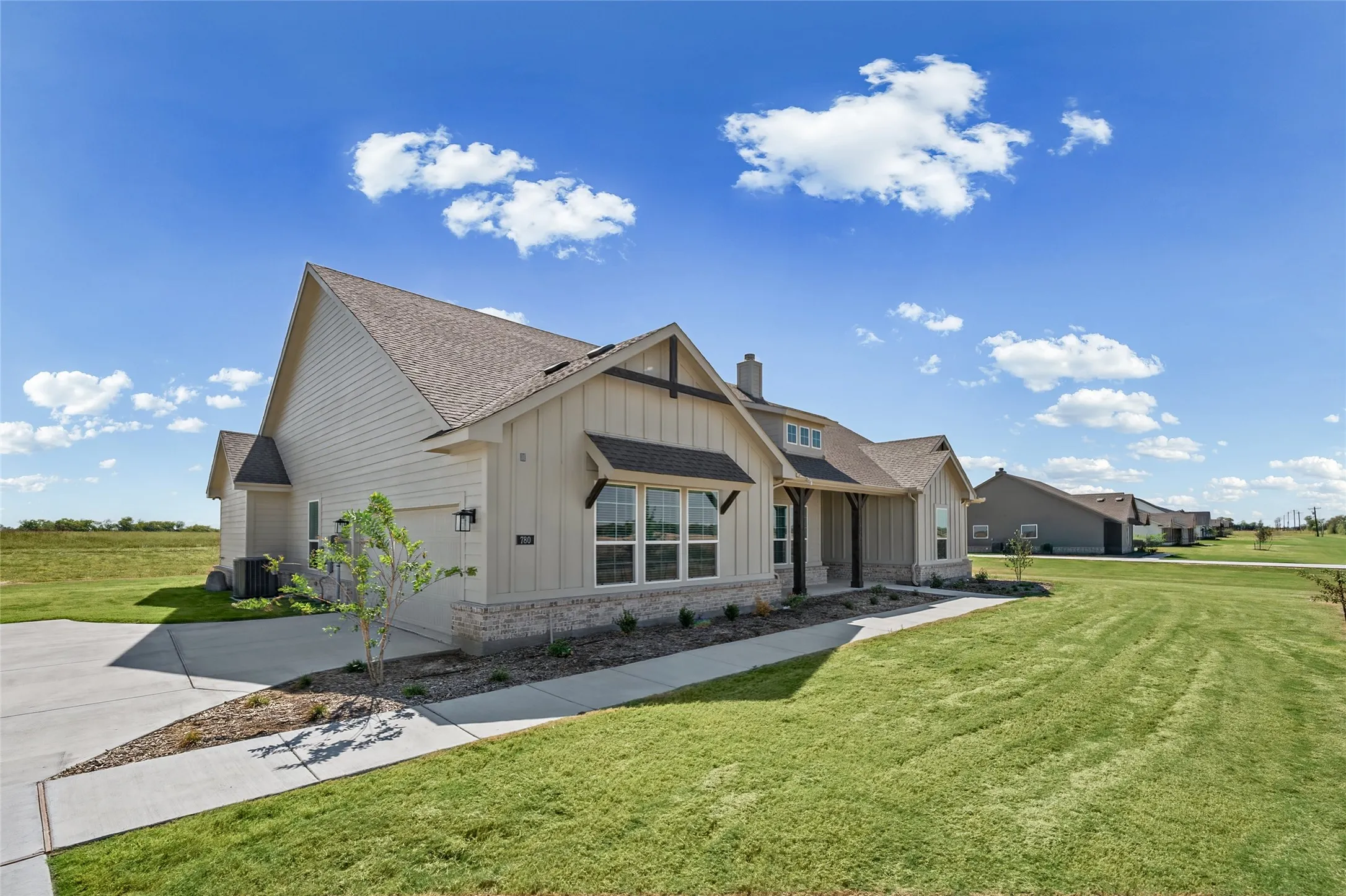 Contemporary home featuring a gabled roof, light-colored siding, stone wainscoting, and a covered entry