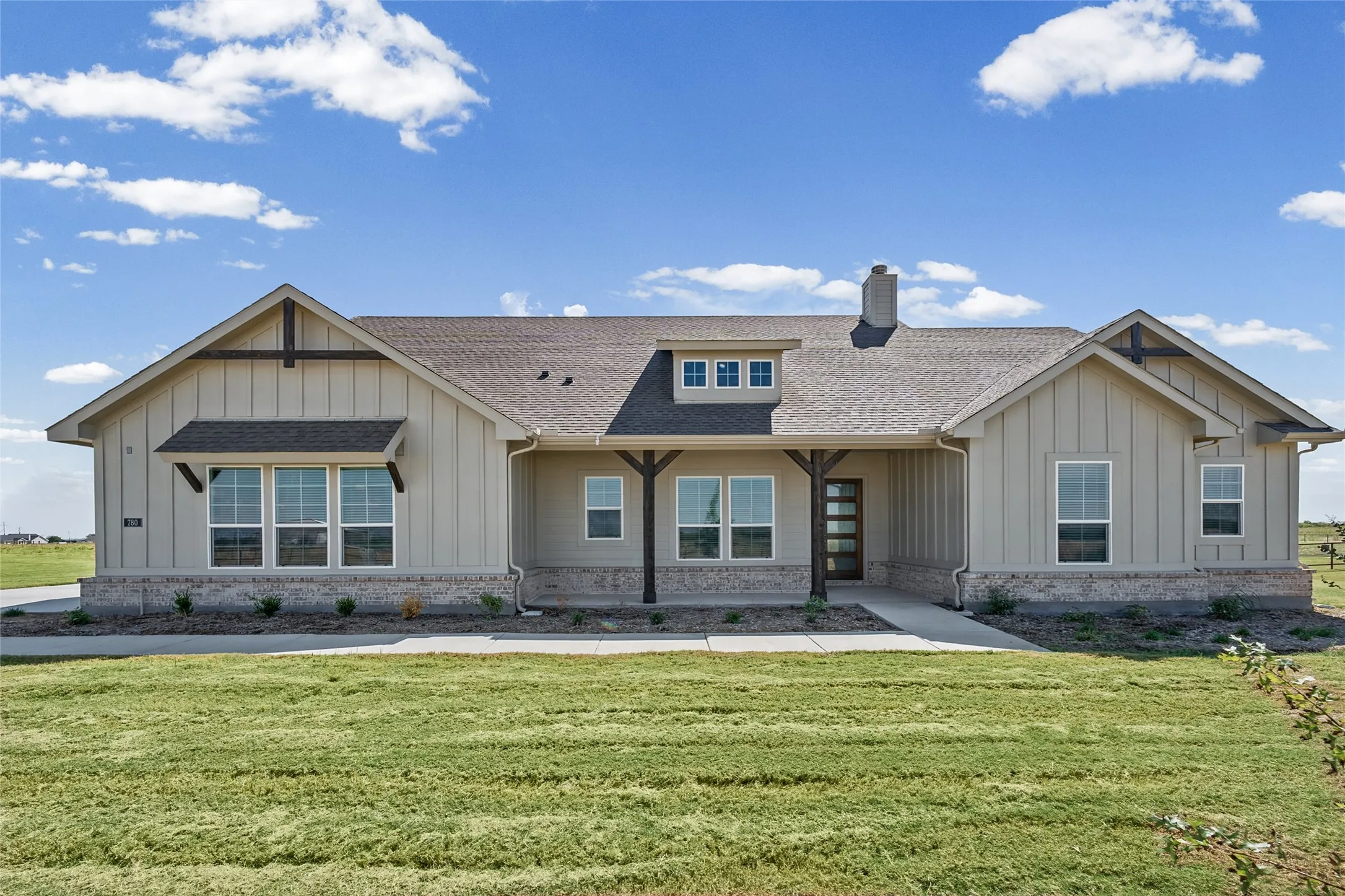 Modern farmhouse exterior with vertical siding, stone skirt, asphalt shingle roof, and a prominent chimney