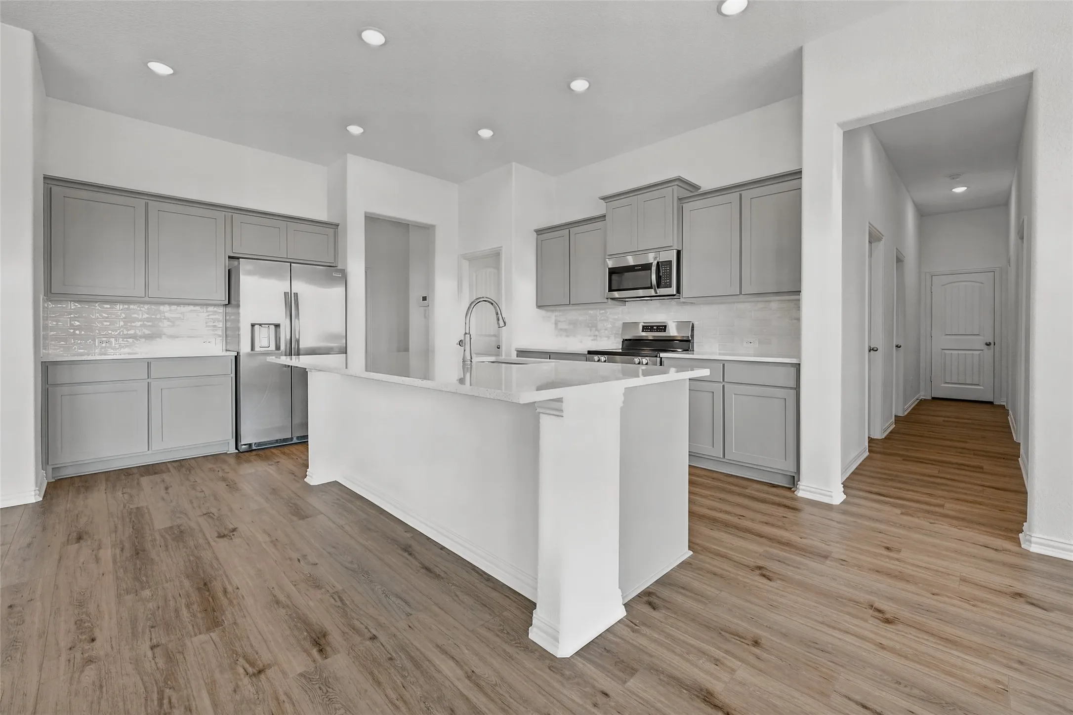 Modern kitchen with gray cabinetry, stainless steel appliances, a center island with sink, white countertops, and wood-finish flooring