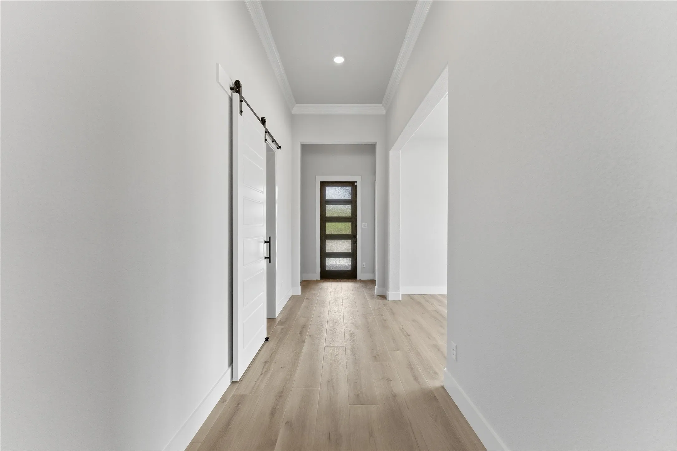 Hallway with a barn door, ornamental molding, light wood-style floors, and recessed lighting