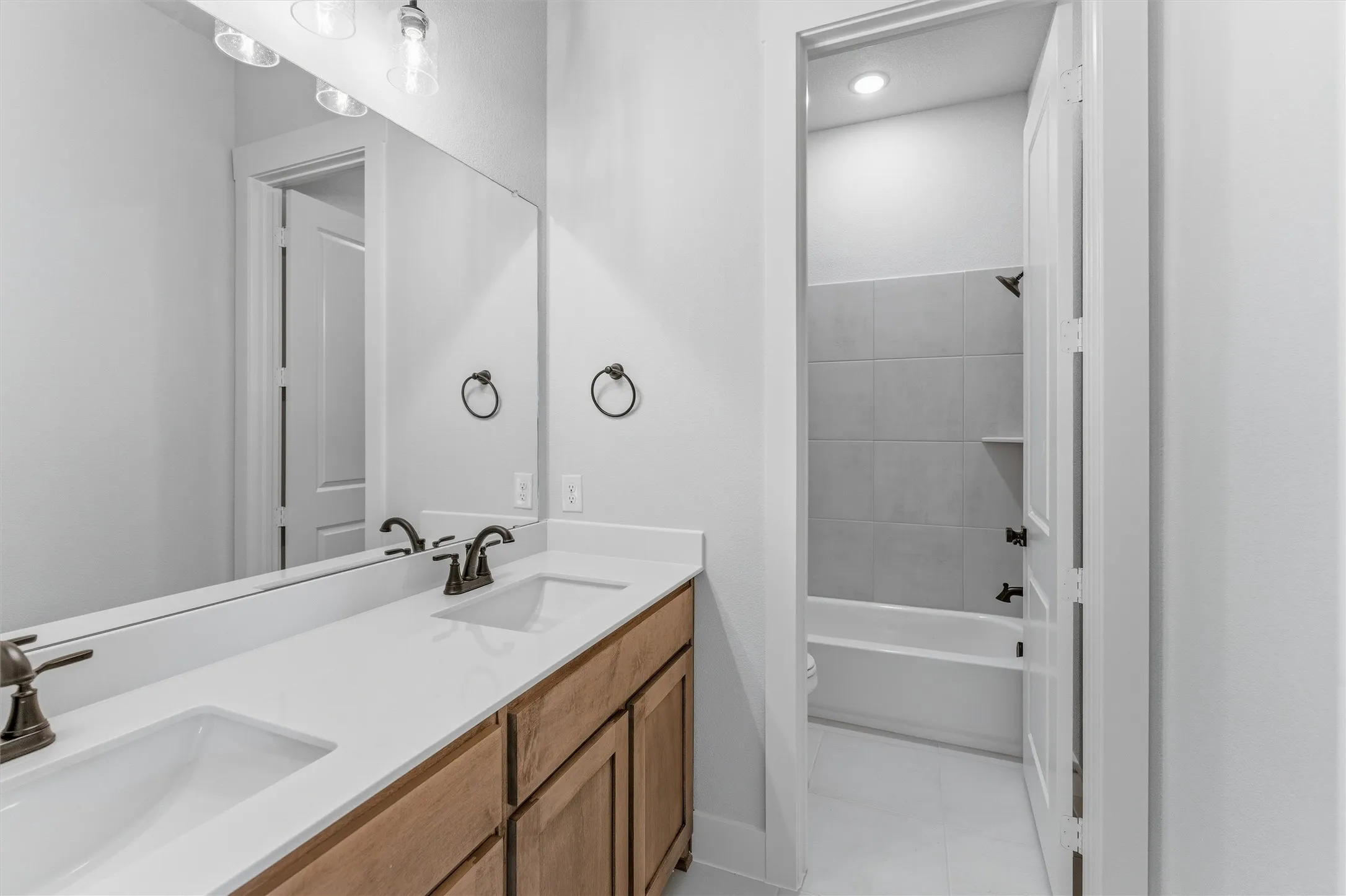 Bathroom featuring double vanity, washtub / shower combination, and light tile patterned flooring