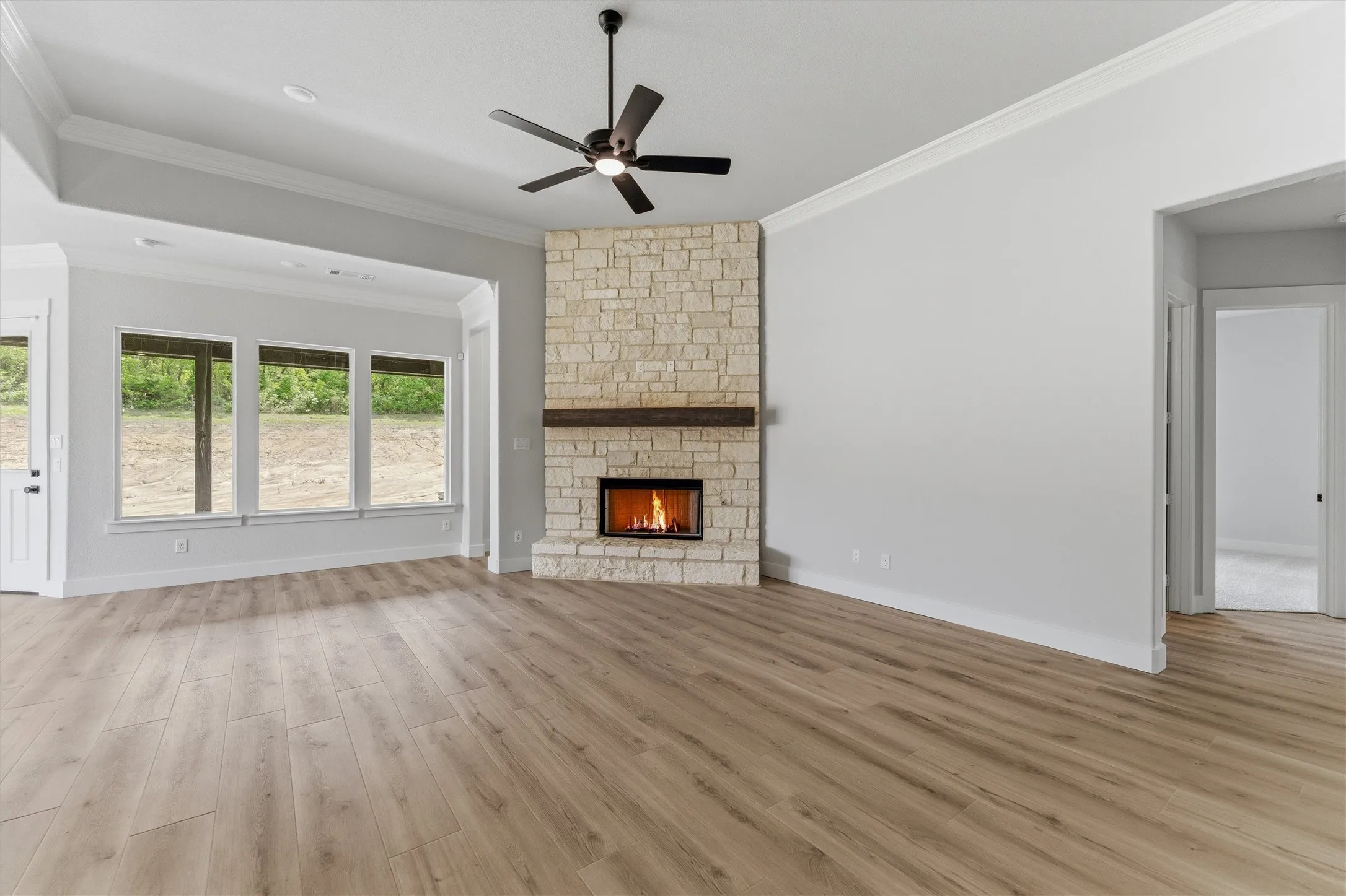Unfurnished living room with light wood-type flooring, a ceiling fan, ornamental molding, and a fireplace