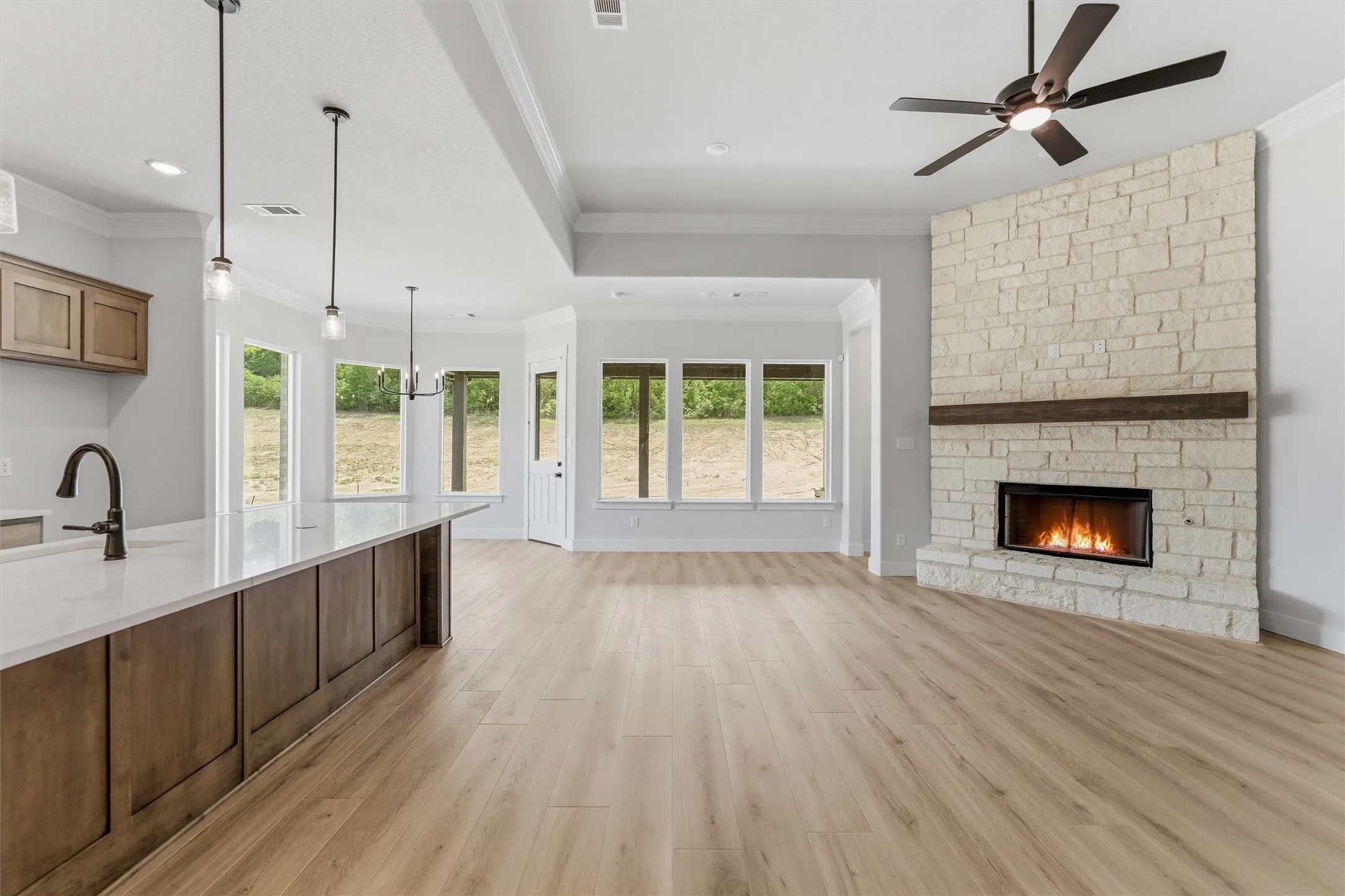 Unfurnished living room with a fireplace, crown molding, light wood-style flooring, a ceiling fan, and healthy amount of natural light