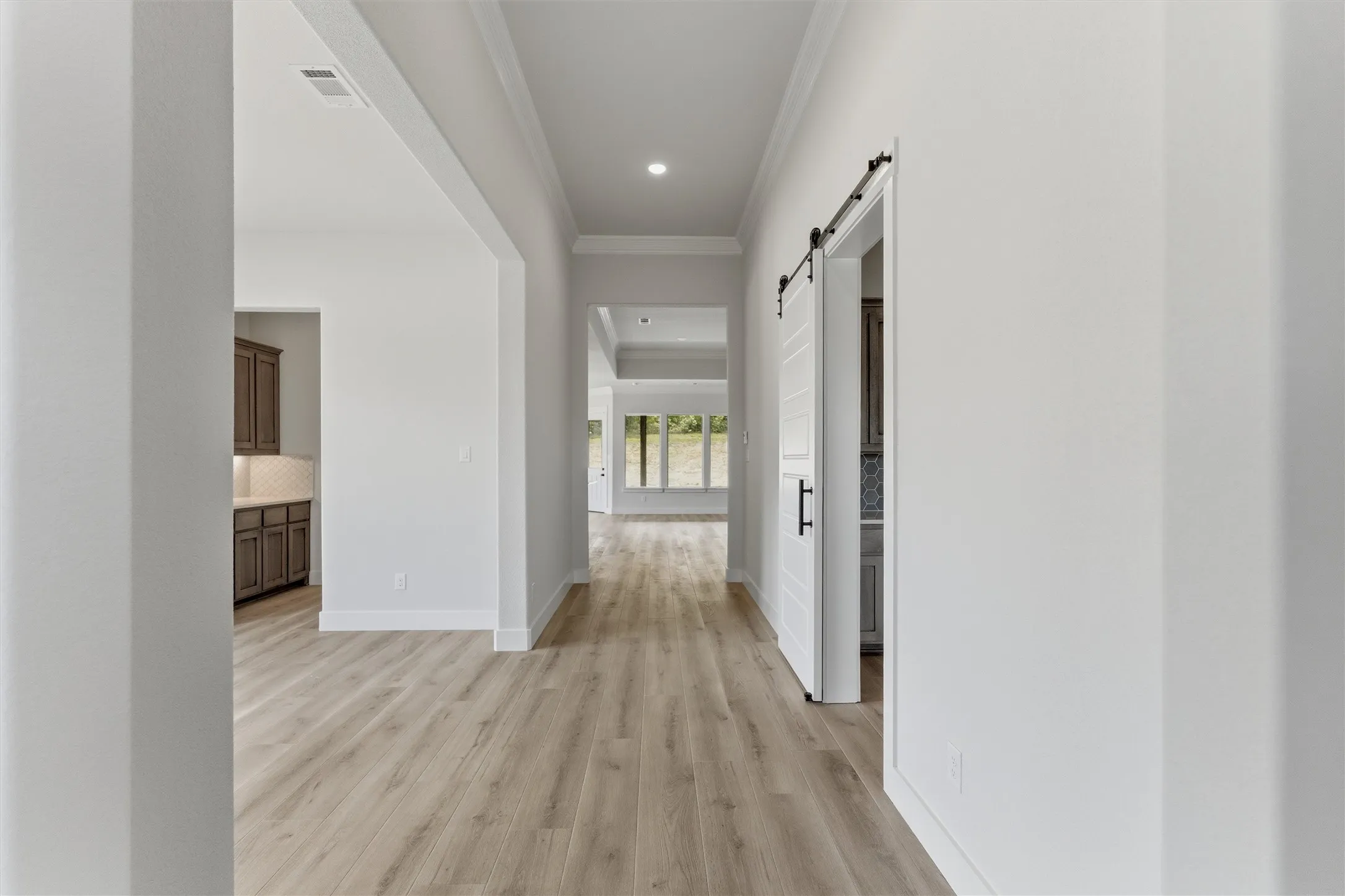 Hallway with a barn door, light wood-type flooring, ornamental molding, and recessed lighting