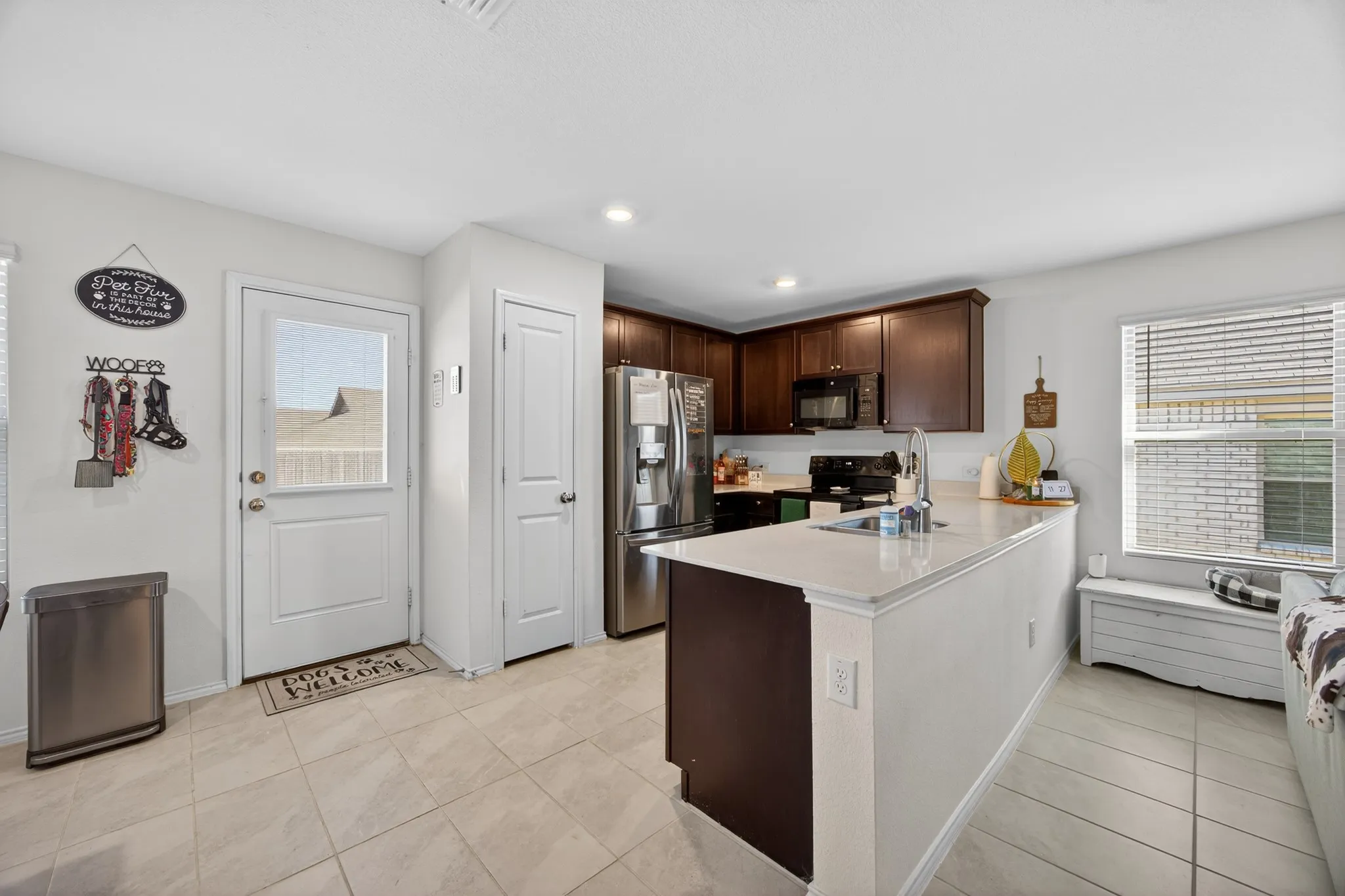 Kitchen with dark brown cabinetry, light countertops, a peninsula, black appliances, and healthy amount of natural light