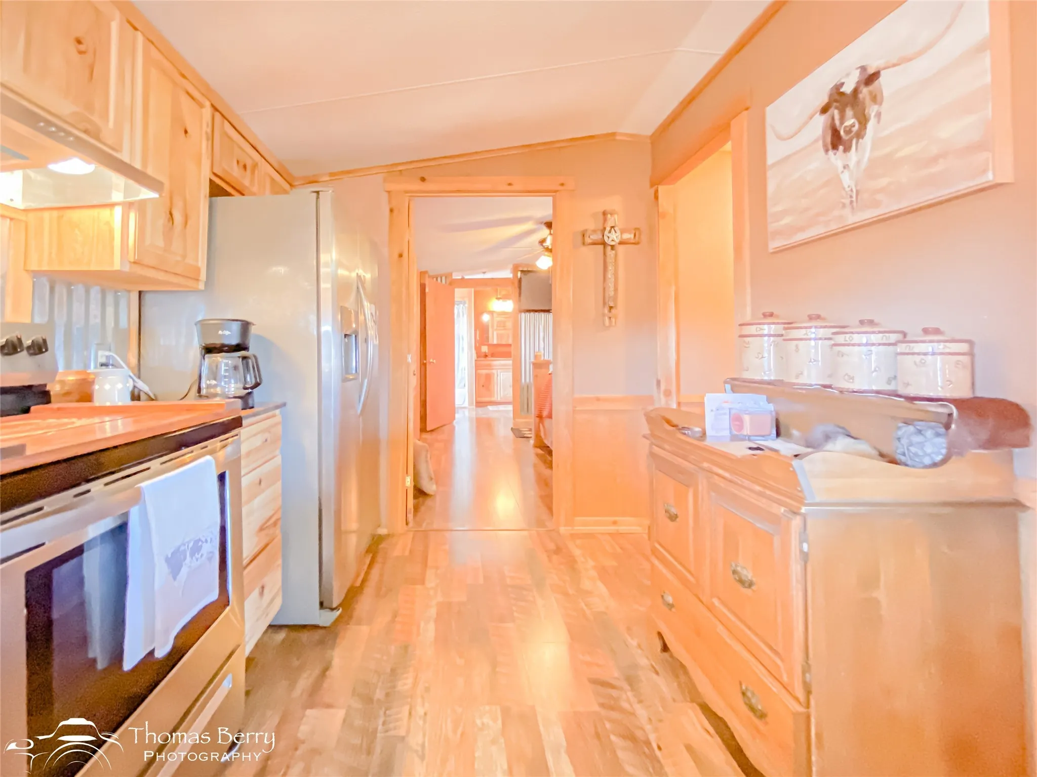 Kitchen featuring stainless steel appliances, light brown cabinets, vaulted ceiling, light wood-style floors, and wainscoting
