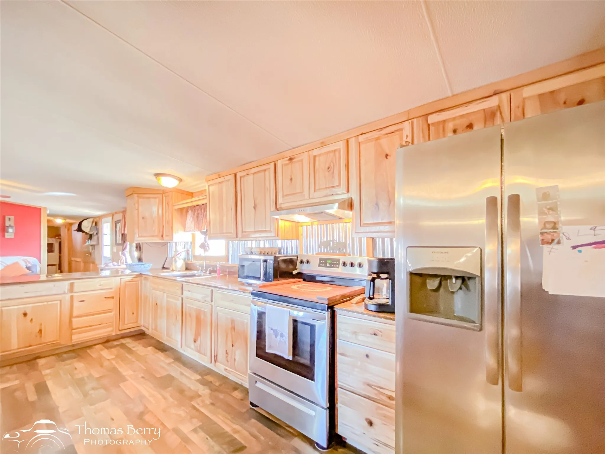 Kitchen featuring light brown cabinetry, stainless steel appliances, light countertops, light wood-type flooring, and under cabinet range hood