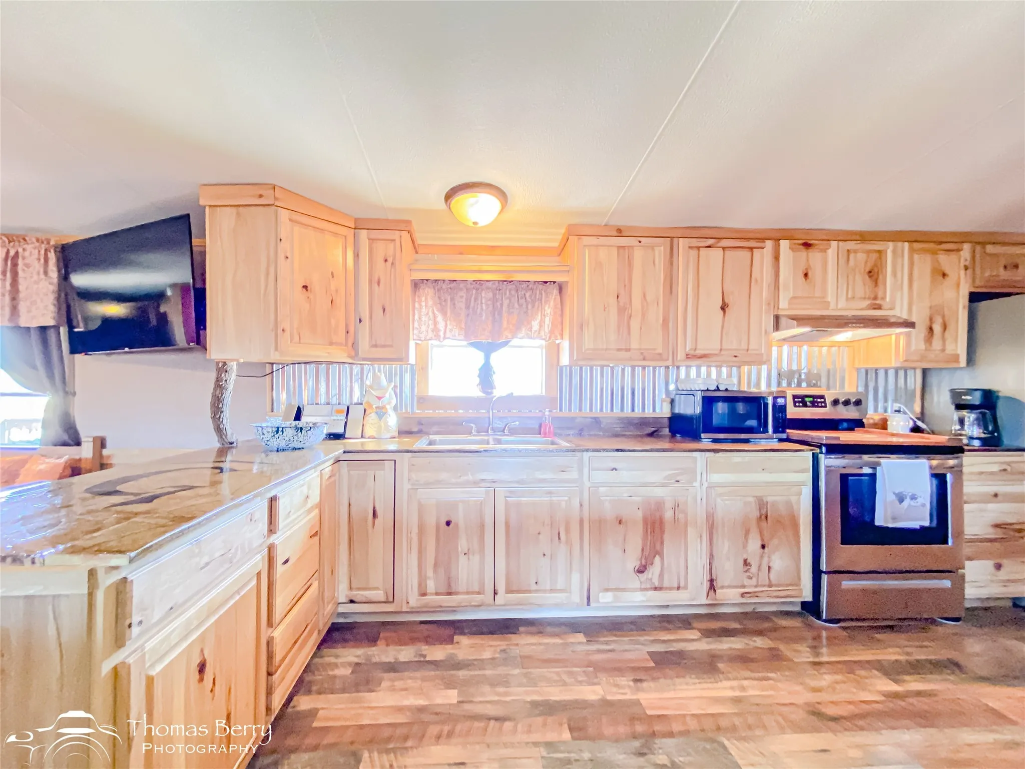 Kitchen with light brown cabinetry, stainless steel range with electric cooktop, light wood-style flooring, light countertops, and under cabinet range hood