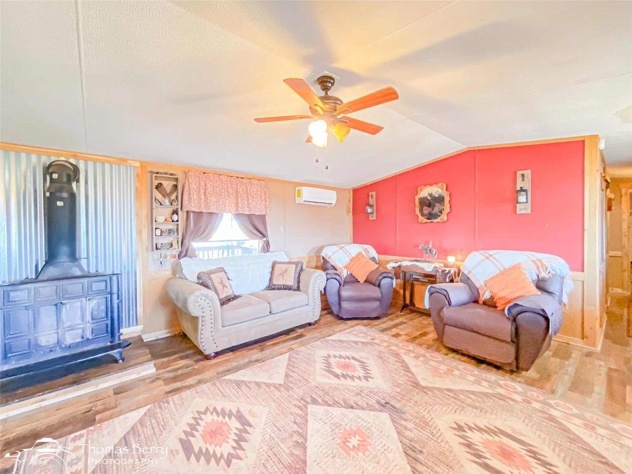 Living area featuring a wood stove, vaulted ceiling, wood finished floors, ceiling fan, and a wall mounted air conditioner
