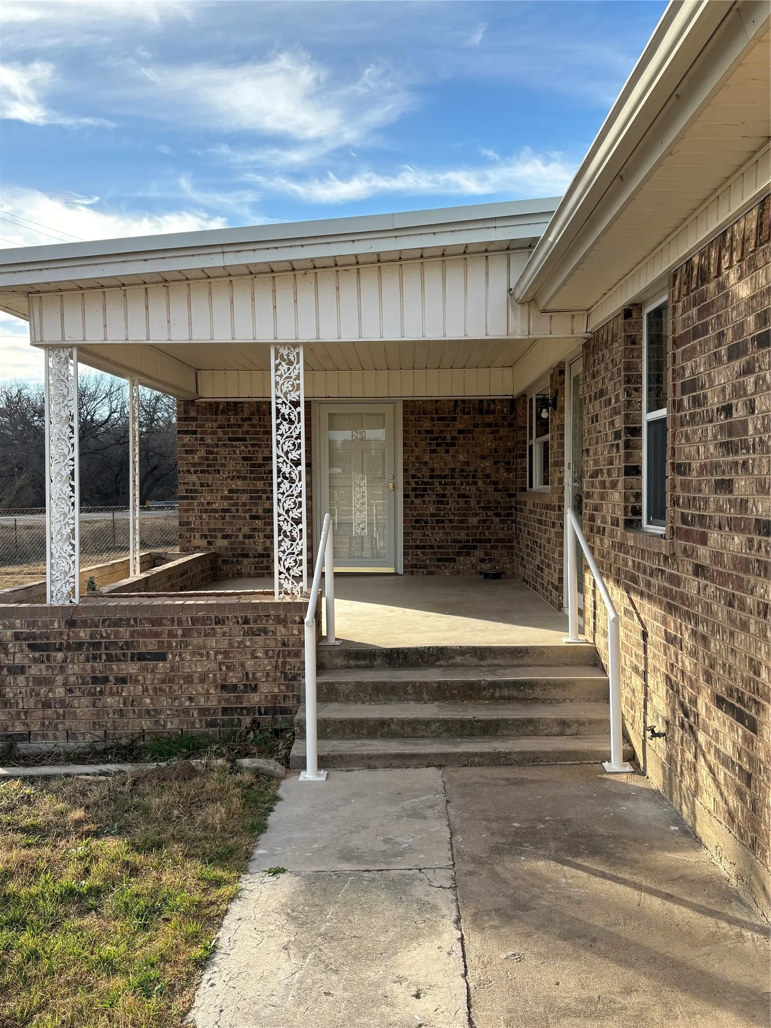 Property entrance featuring brick siding and covered front porch. Fresh paint on the railings, metal beams and doors.
